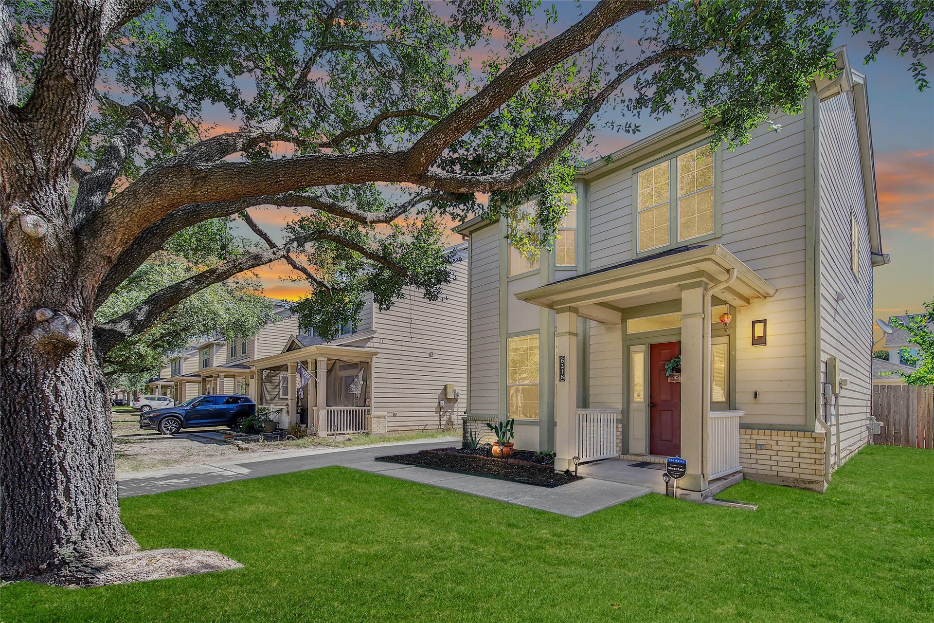 Inviting home framed by a beautiful shade tree with covered front porch. Grass is digitally enhanced.