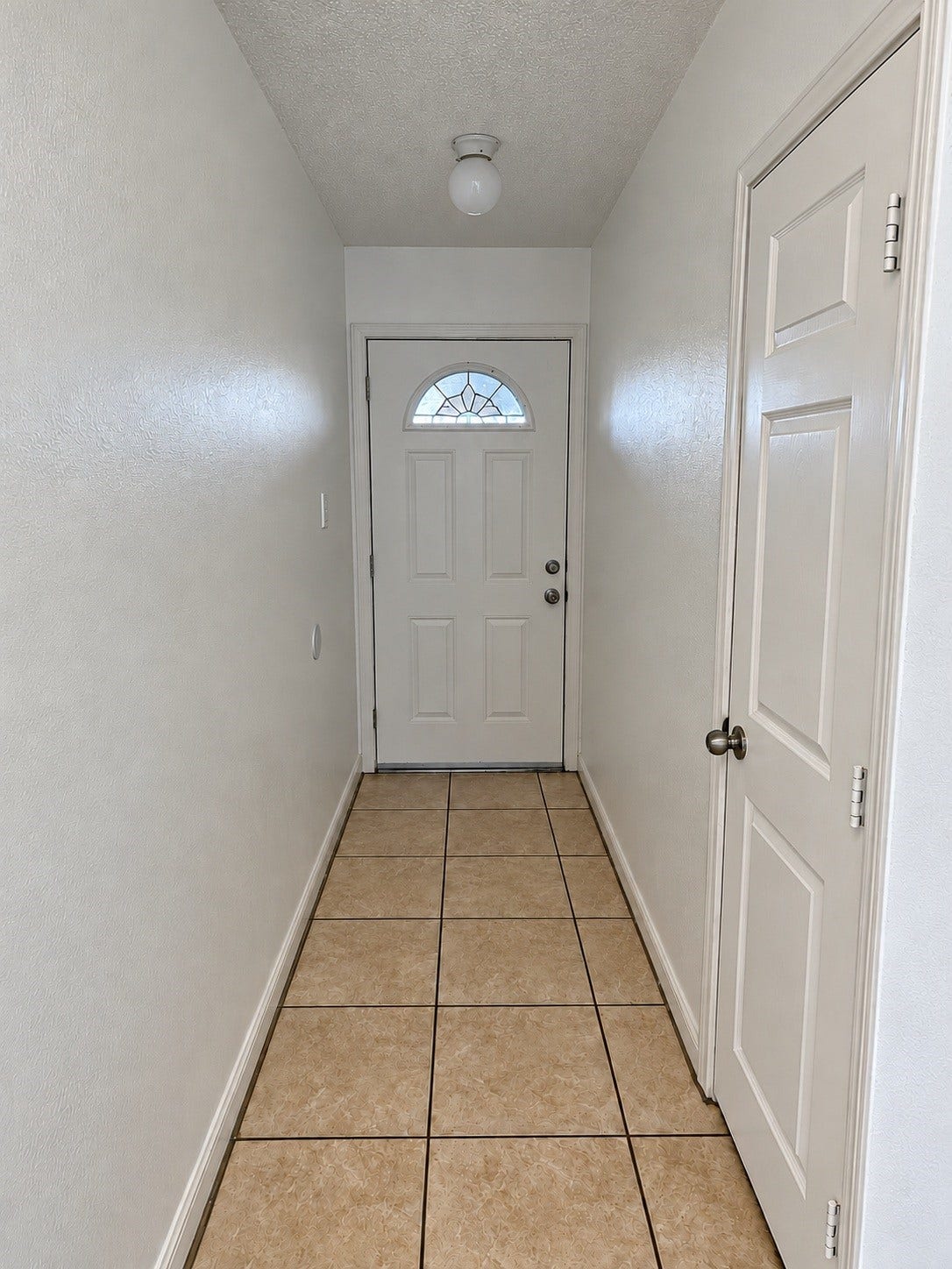 Interior entryway featuring neutral walls, tile flooring, and a front door with decorative glass detailing.