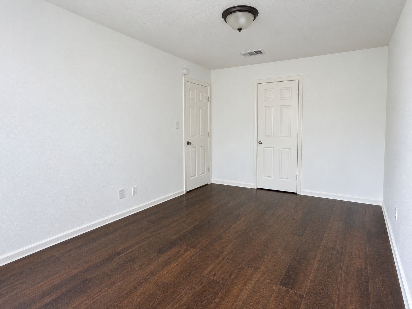 Third party highlights the rich, dark wood-look flooring, neutral walls, and spacious layout, offering flexibility for bedroom furnishings, a home office, or a guest room.