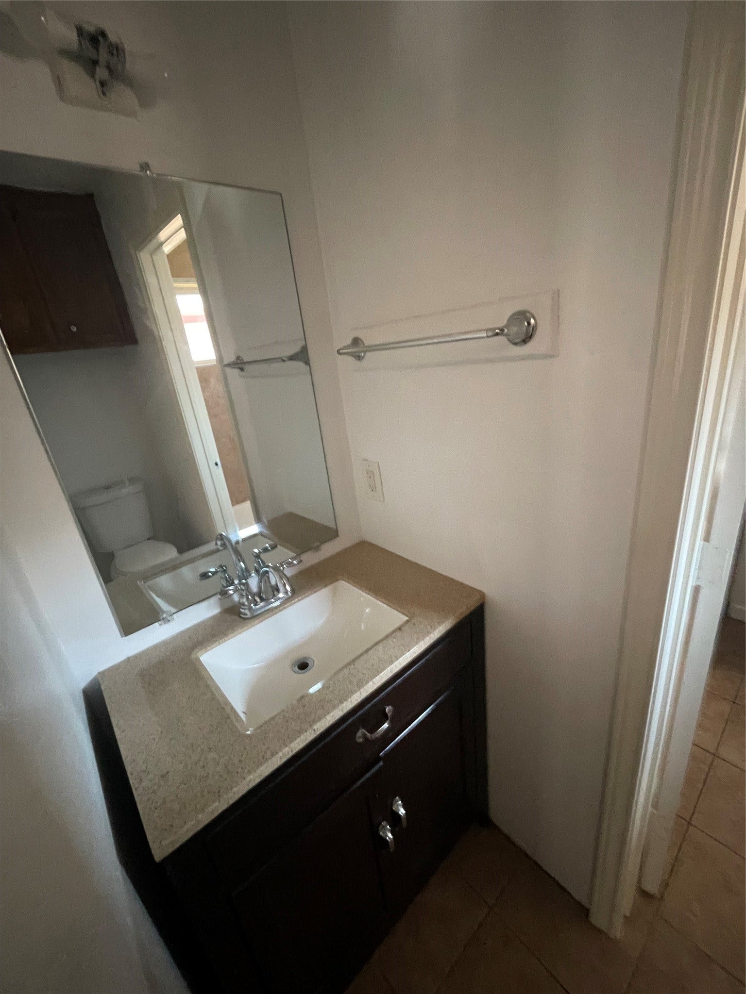 Half bathroom featuring a modern vanity with dark cabinetry, a white countertop, a large mirror, and neutral wall colors. A functional space that connects to the full bathroom.