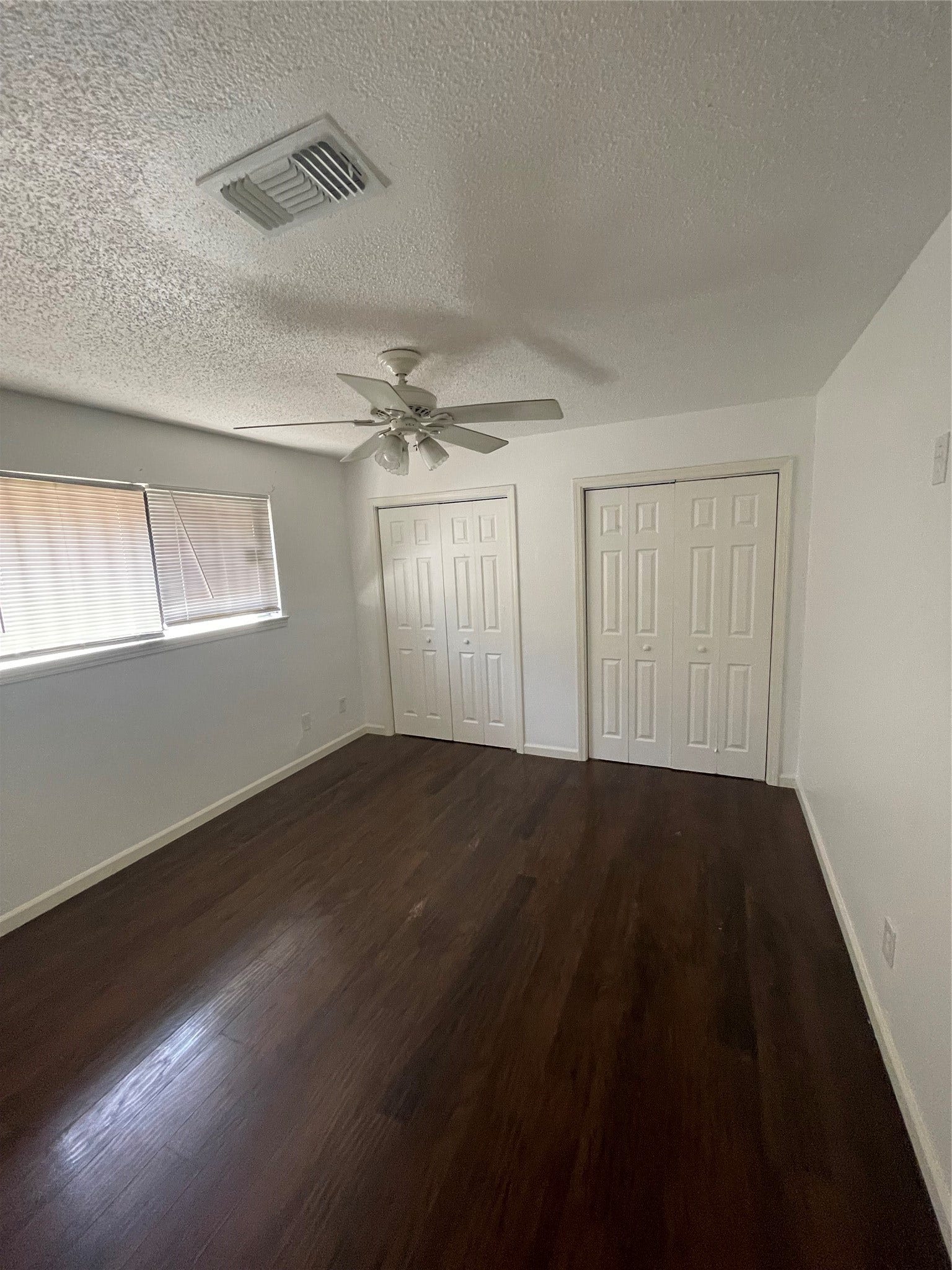 Spacious primary bedroom featuring wood look flooring, neutral wall colors, a ceiling fan, two closets offering additional storage, and windows that provide natural light. A comfortable and versatile space ready for your personal touch.