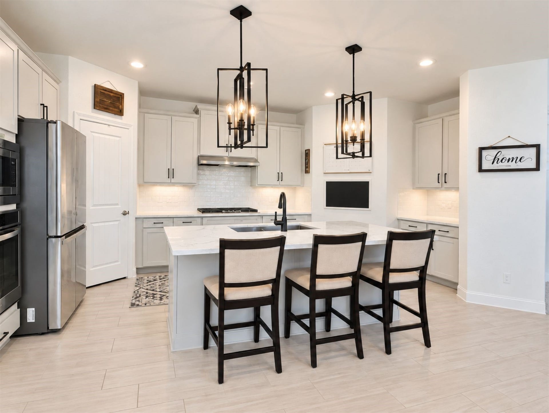 8822 SPINNING MILL DRIVE, Missouri City, TX 77459 THE KITCHEN FEATURES WHITE CABINETRY, A LARGE ISLAND WITH BAR SEATING, AND TWO STATEMENT PENDANT LIGHTS.