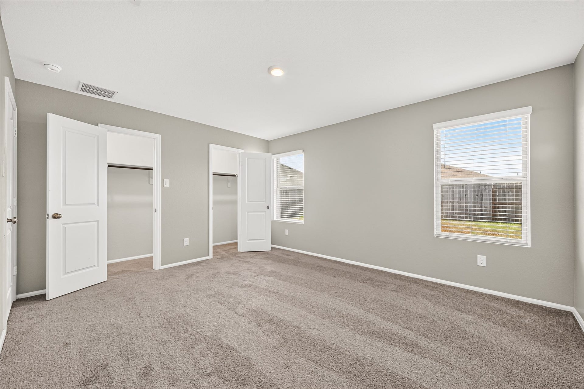 19494 Rosali Meadow Drive, New Caney, TX 77357 Spacious bedroom with newly installed carpet flooring, neutral walls, and abundant natural light from two large windows, featuring dual closets for ample storage.