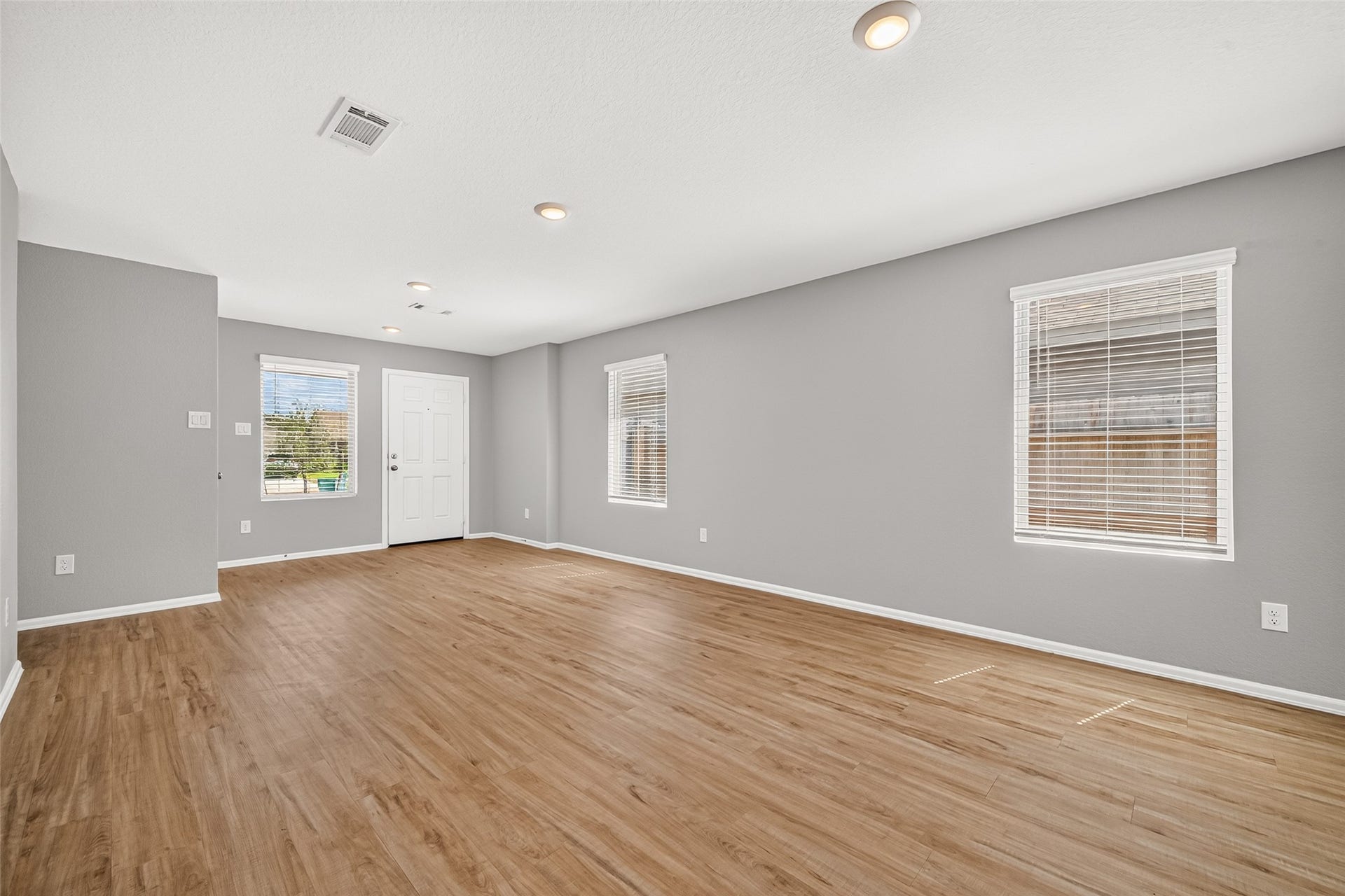 19494 Rosali Meadow Drive, New Caney, TX 77357 Living area with sleek wood flooring, neutral gray walls, and abundant natural light from multiple windows, creating a welcoming atmosphere.