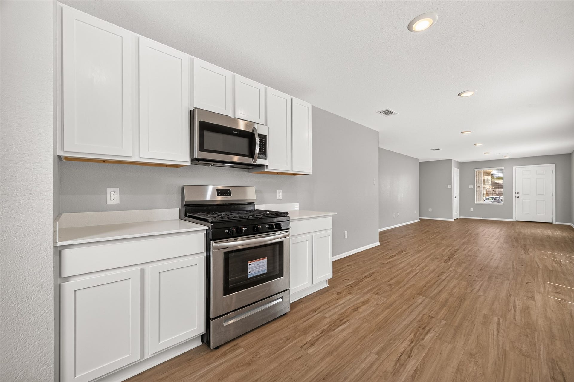 19494 Rosali Meadow Drive, New Caney, TX 77357 Open-concept kitchen and living area featuring sleek stainless steel appliances, modern white cabinetry, and inviting hardwood floors.