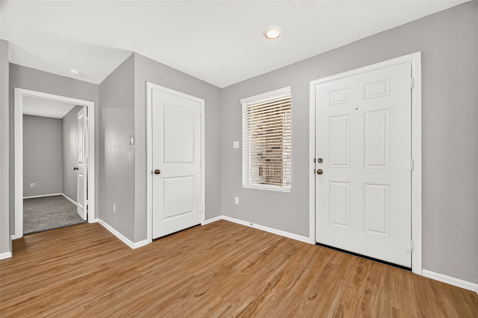 19494 Rosali Meadow Drive, New Caney, TX 77357 Bright entryway featuring sleek hardwood floors and fresh gray walls, leading to a cozy carpeted room.