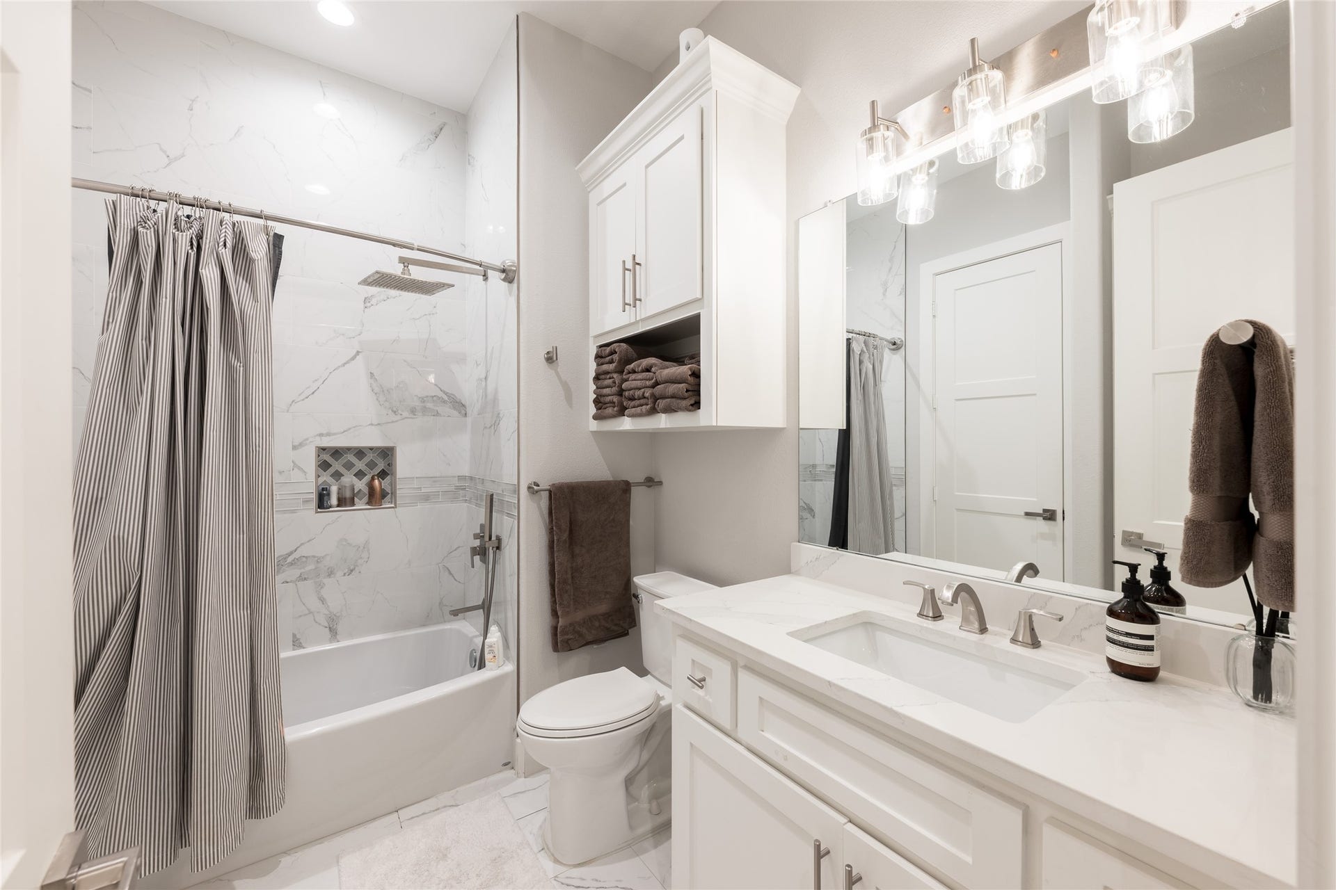 906 Knox Street, Houston, TX 77007 Clean lines and a light, refined palette define this secondary bath, complete with a spacious vanity, built-in storage, and tiled tub surround.
