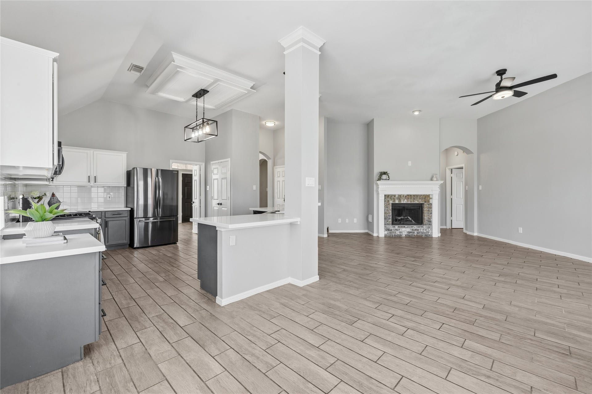 4011 Grayson Court, Missouri City, TX 77459 Spacious open-concept living area with modern kitchen, sleek black appliances, and stylish tile flooring, complemented by a cozy fireplace and elegant ceiling fan.