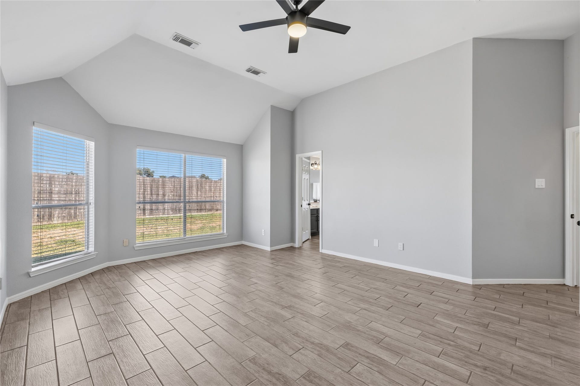 4011 Grayson Court, Missouri City, TX 77459 Spacious primary bedroom with vaulted ceilings, large windows for natural light, sleek tile flooring, and a ceiling fan, leading to an adjoining the primary bath.