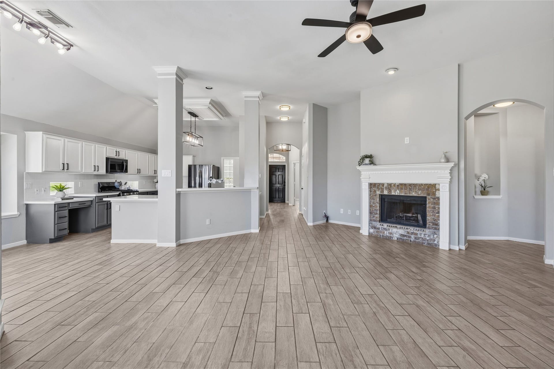 4011 Grayson Court, Missouri City, TX 77459 Spacious open-concept living area featuring sleek wood-look tile flooring, a modern kitchen with stainless steel appliances, and a cozy fireplace with elegant stone accents.