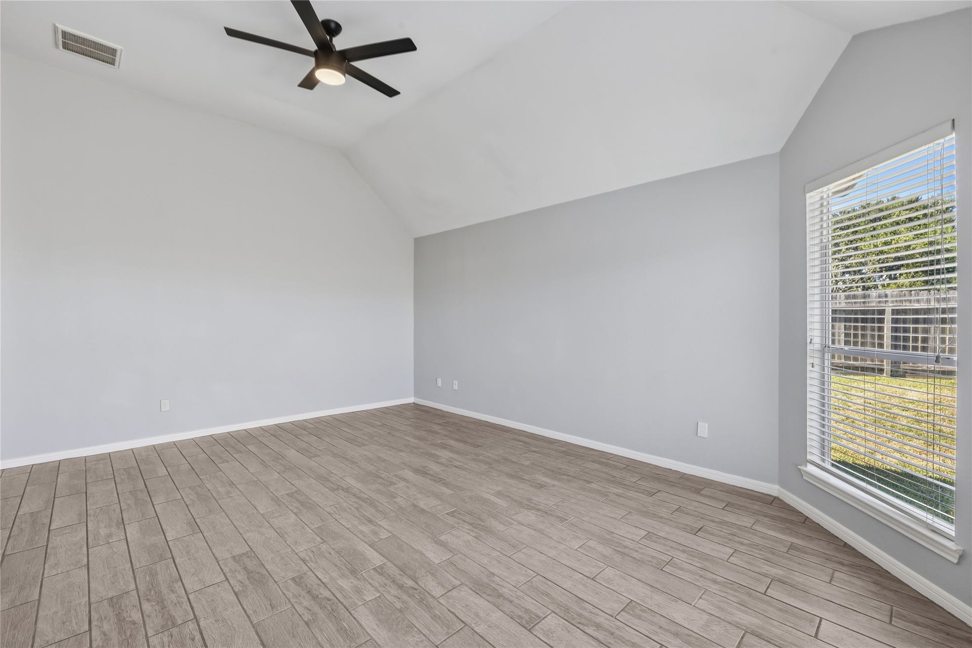 4011 Grayson Court, Missouri City, TX 77459 Spacious room with high ceilings, elegant wood-look tile flooring, a modern ceiling fan, and abundant natural light from a large window overlooking the backyard.