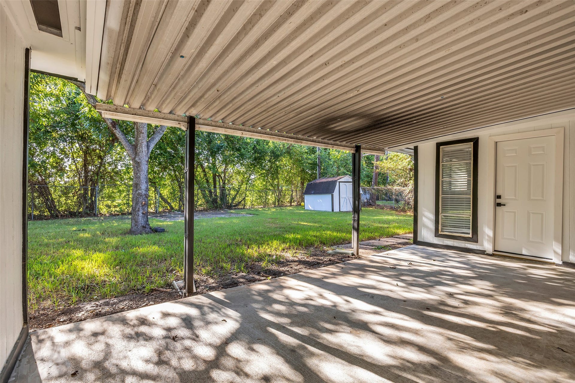 Relax in the shade on the covered patio, overlooking a large backyard with mature trees.