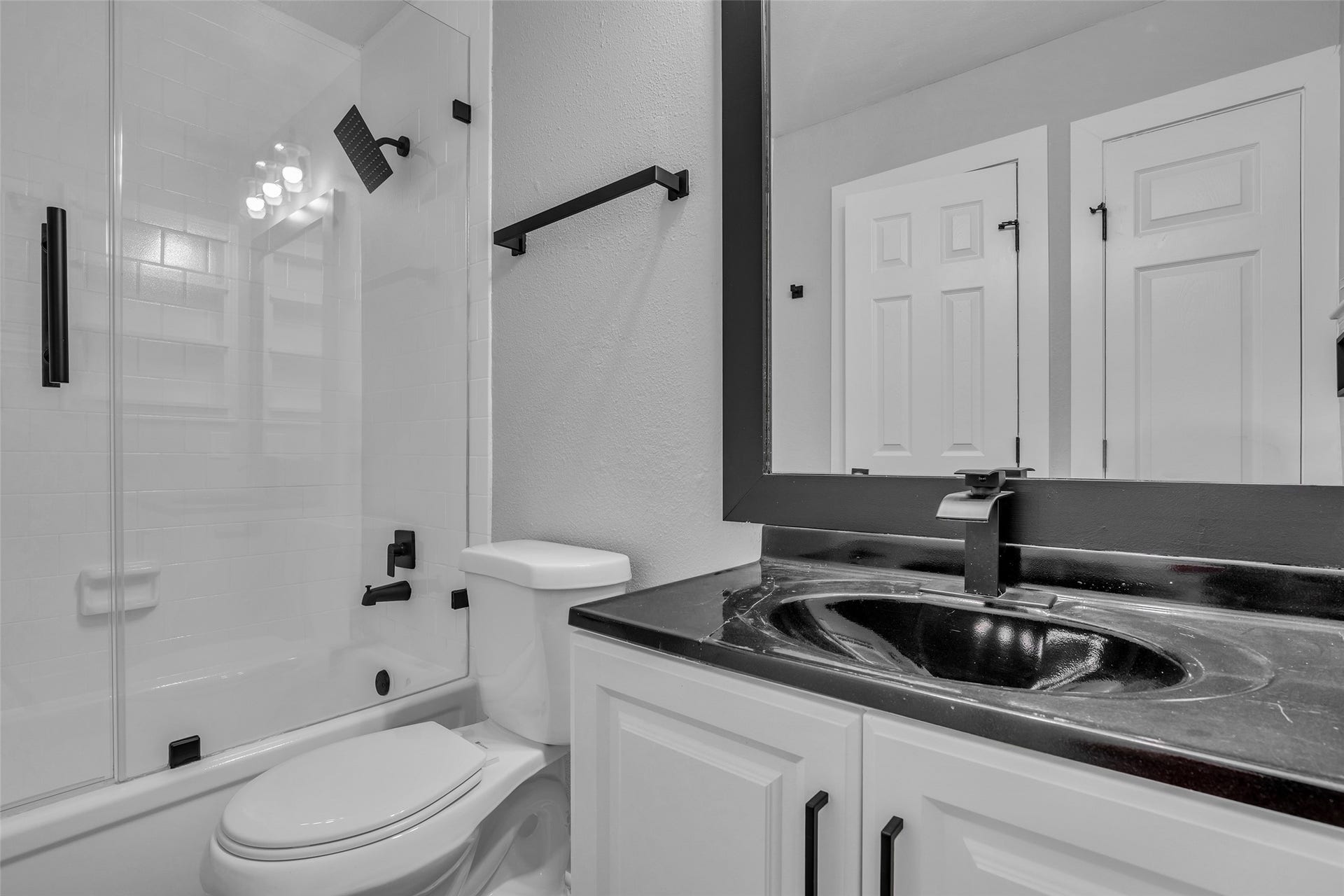 A bath with a glass-enclosed tub/shower, white vanity and matte black fixtures.