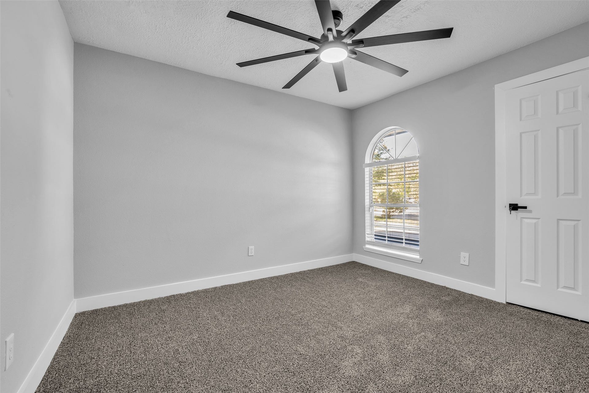 A cozy secondary bedroom with an arched window and a ceiling fan, ready for guests or a home office.