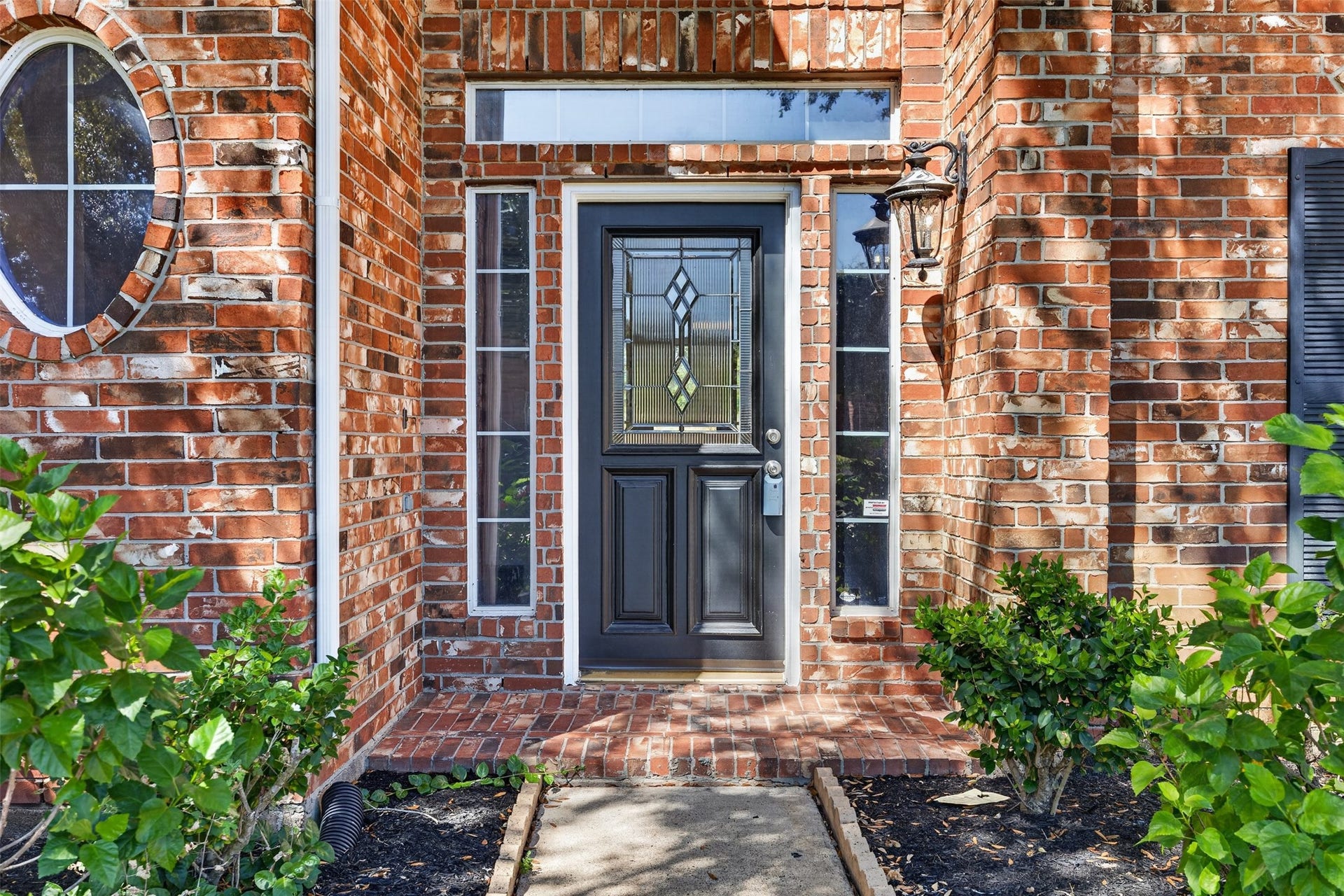 3114 Brannon Hill Lane, Sugar Land, TX 77479 Charming brick entryway highlighted by a stylish front door with decorative glass panels, framed by lush greenery and elegant lighting.
