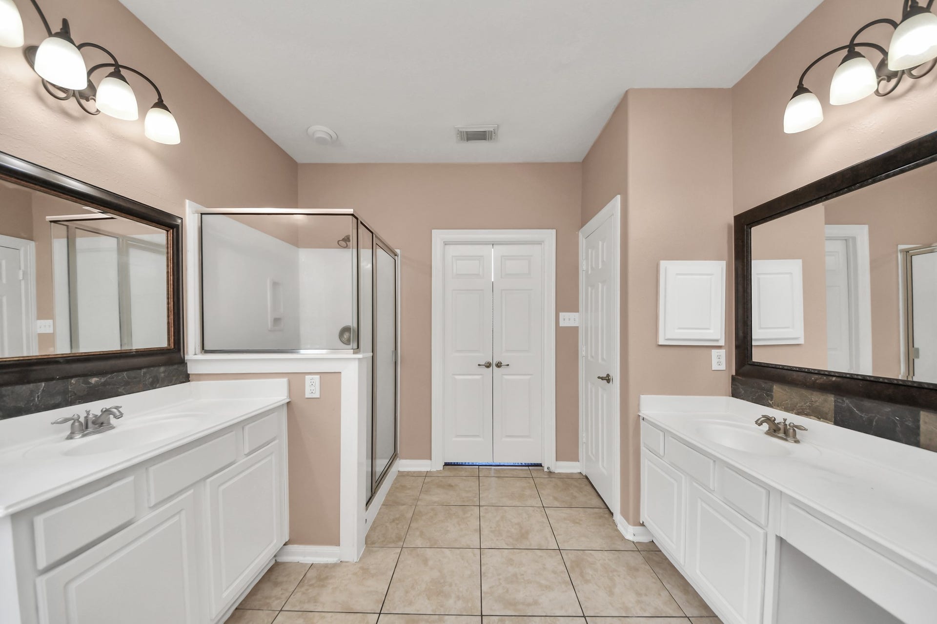 Spacious bathroom featuring dual vanities, a glass-enclosed shower, and elegant lighting, offering a bright and functional space.