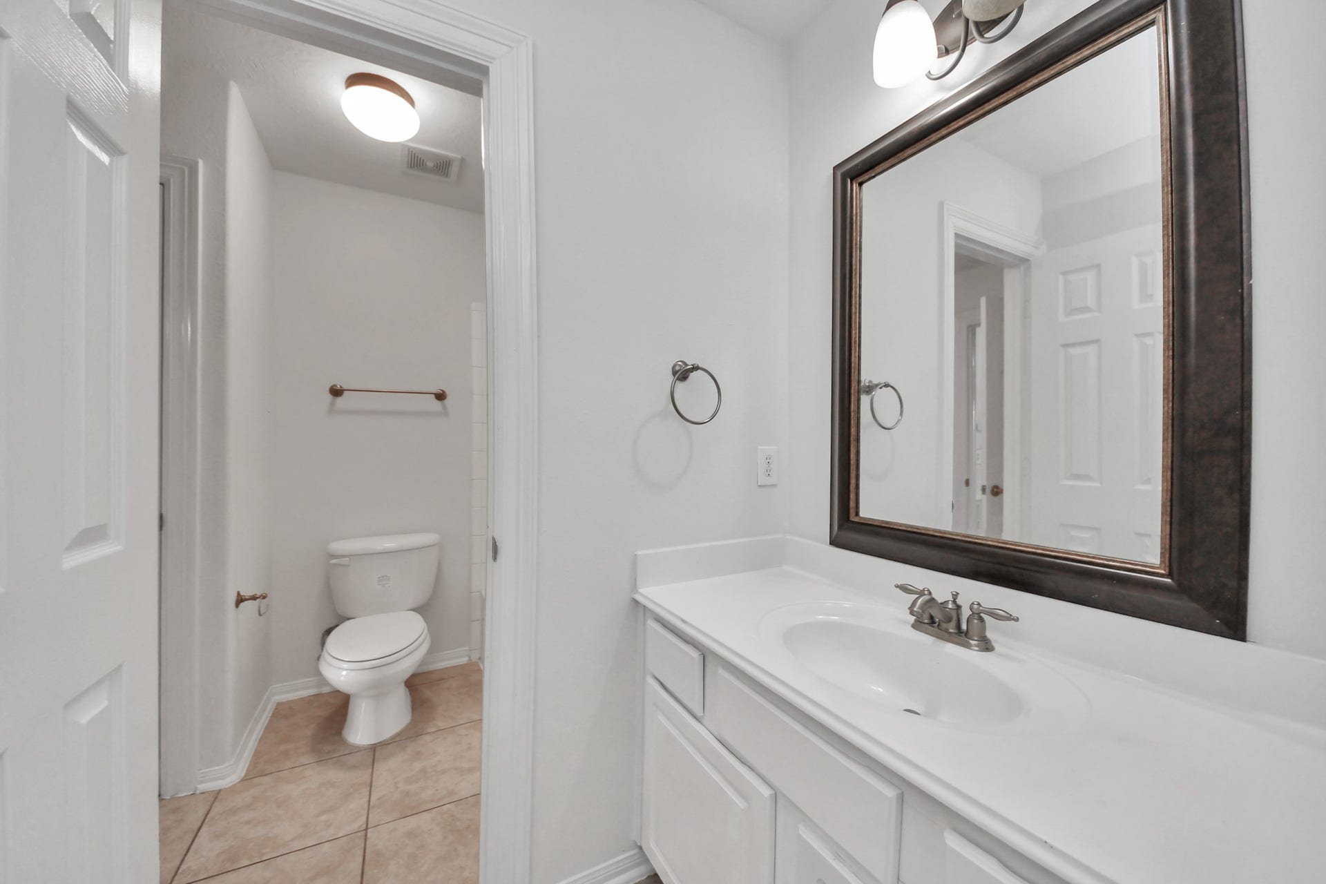 Bright bathroom featuring a large vanity with ample counter space, a stylish framed mirror, and a separate toilet area for added privacy.