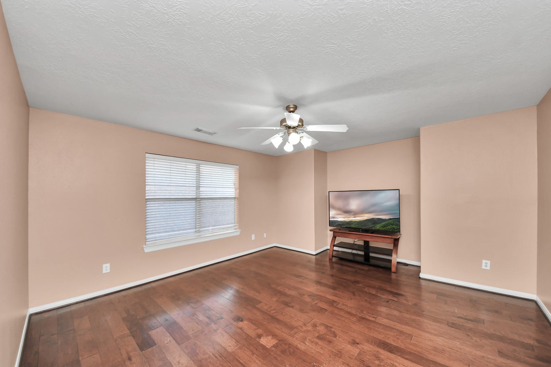 Spacious MEDIA /GAME ROOM area with warm hardwood floors, abundant natural light from a large window, and a ceiling fan for comfort.