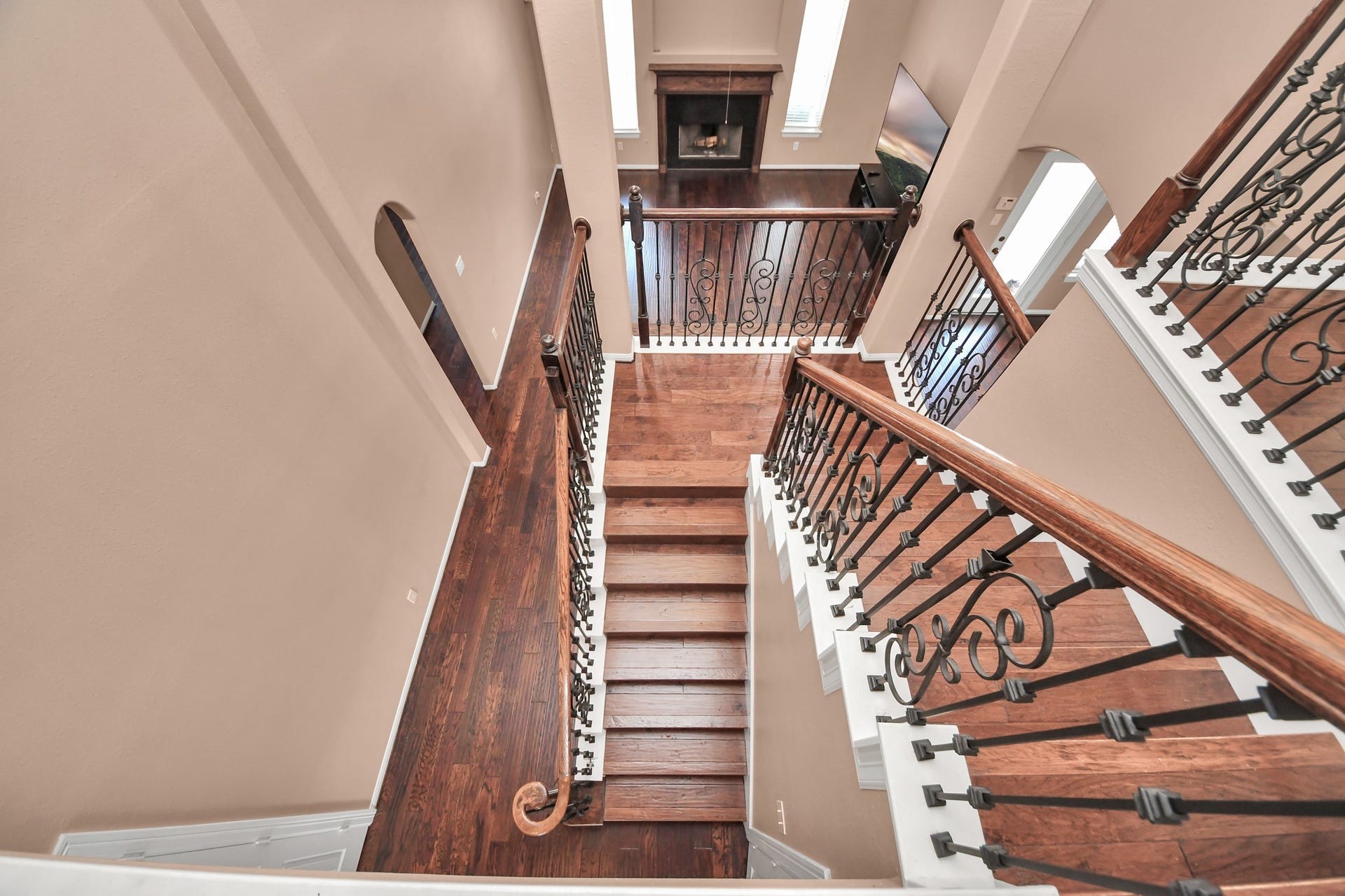 Elegant staircase with rich wood flooring and wrought iron railings, leading to a spacious living area with high ceilings and a cozy fireplace.