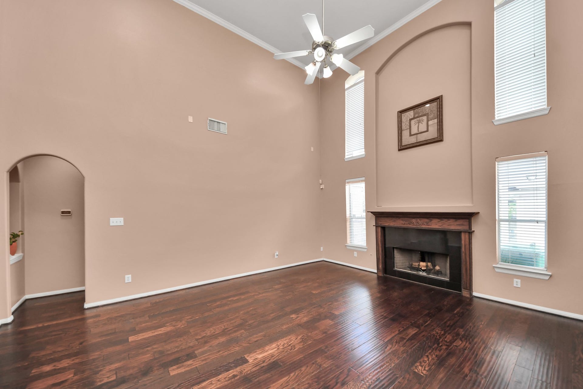 Spacious living room with soaring ceilings, elegant dark hardwood floors, and a cozy fireplace, framed by tall windows for ample natural light.
