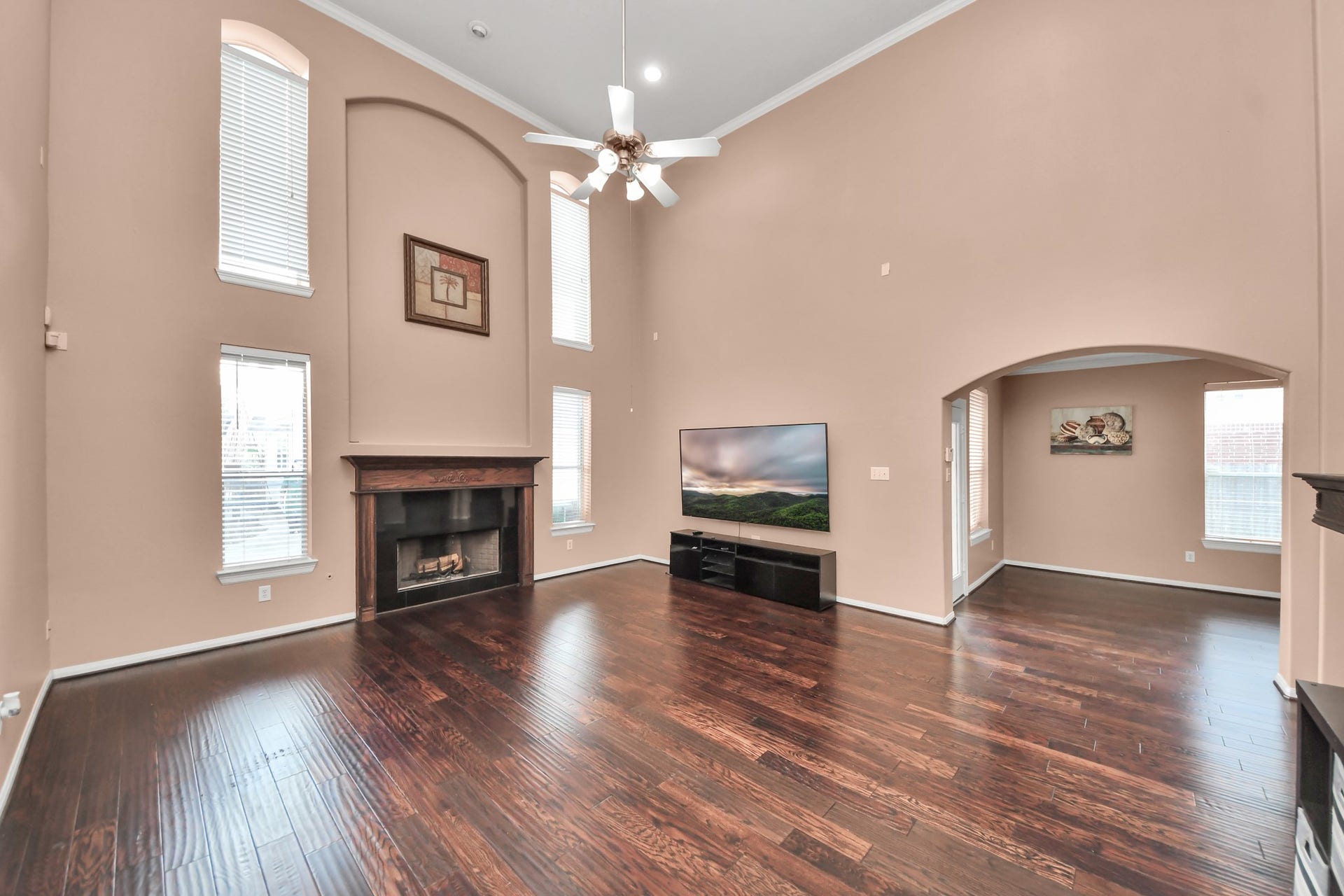 Spacious living room with soaring ceilings, rich hardwood floors, and abundant natural light, featuring a cozy fireplace and elegant arched entryway.