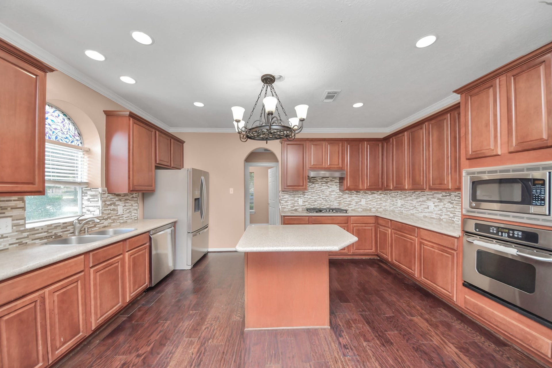 Spacious kitchen featuring rich wood cabinetry, sleek stainless steel appliances, and elegant tile backsplash, complete with a central island and stylish chandelier.
