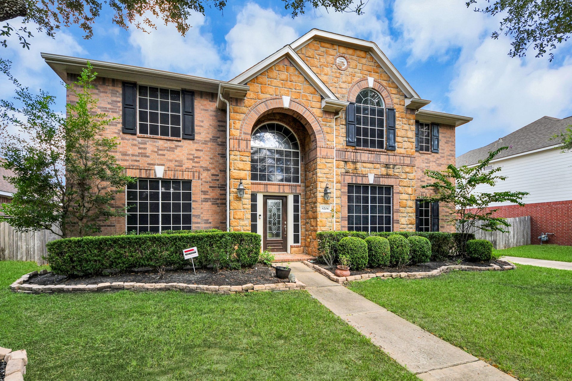 Stunning two-story home with a blend of brick and stone facade, featuring a grand entrance, manicured landscaping, and large windows for abundant natural light.
