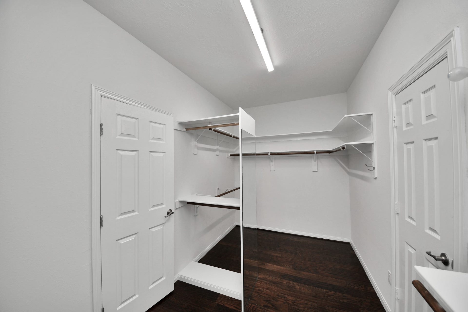 Spacious walk-in closet with dark hardwood floors, ample shelving, and hanging space, perfect for organizing your wardrobe.