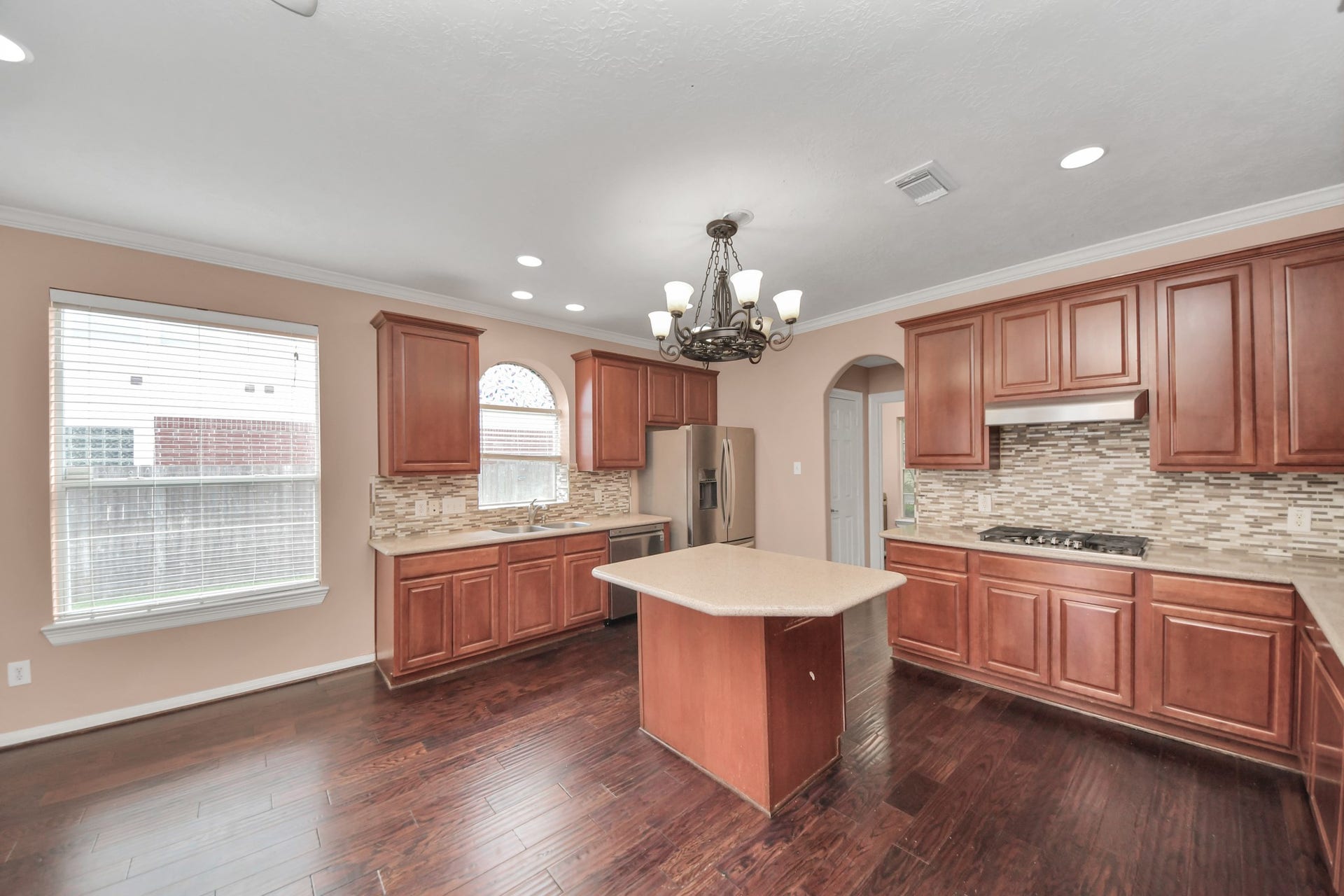 Spacious kitchen with elegant wood cabinetry, a central island, and modern stainless steel appliances, complemented by a stylish tile backsplash and rich hardwood floors.