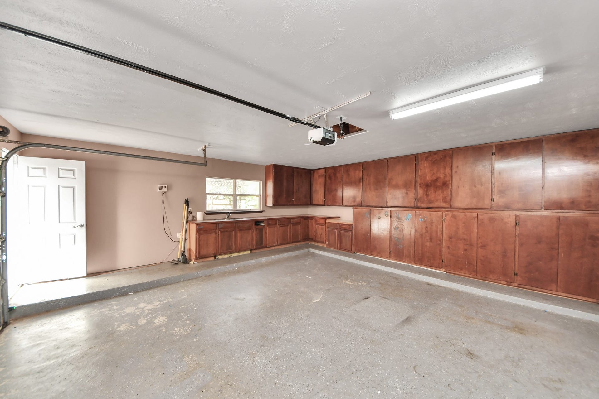 Spacious garage featuring abundant built-in cabinetry for ample storage, a convenient side door, and bright overhead lighting.