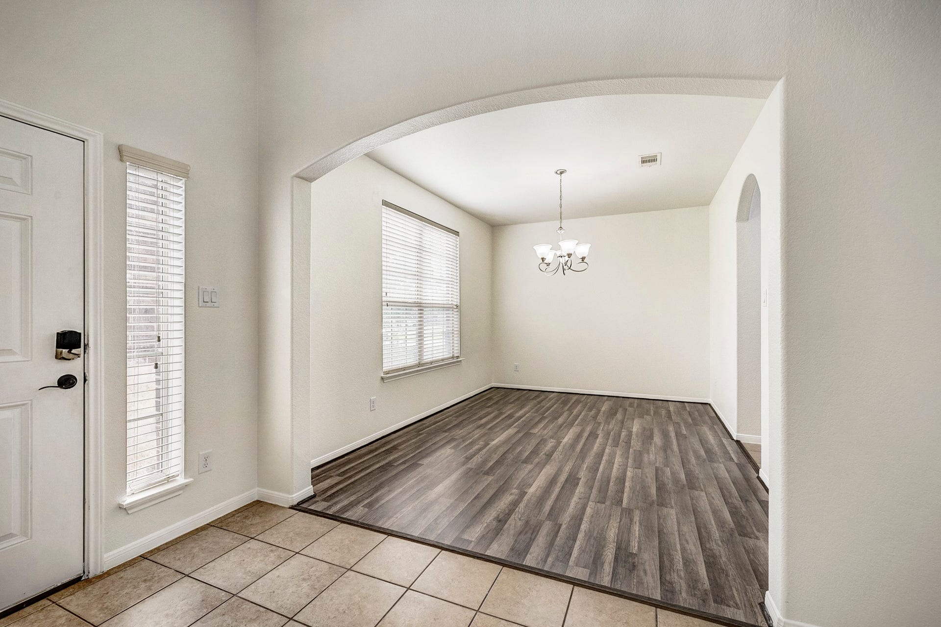 33227 Greenfield Forest Drive, Magnolia, TX 77354 Bright and inviting entryway featuring elegant tile flooring transitioning to wood-look floors, with an arched opening leading to a spacious dining area enhanced by a charming chandelier.