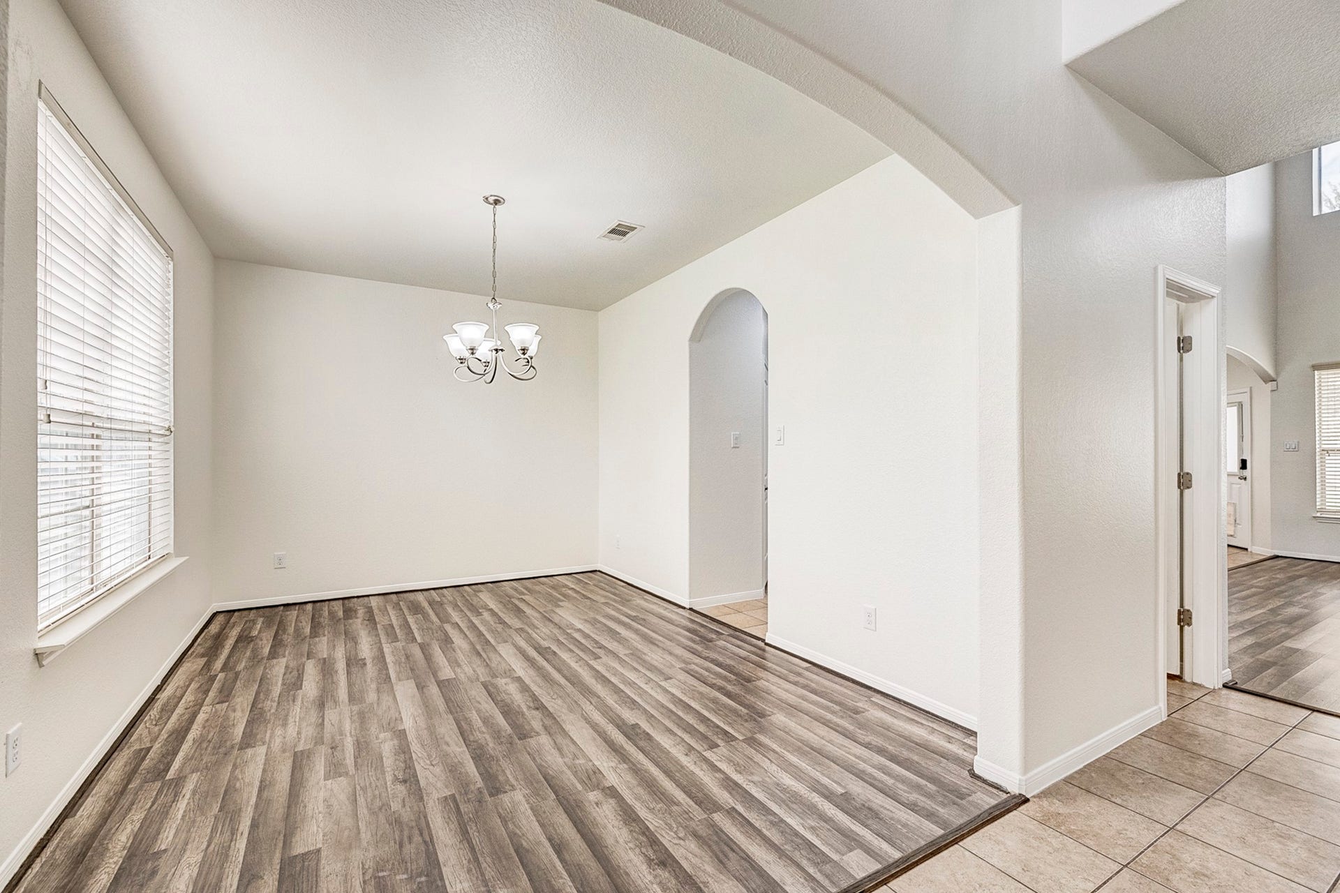 33227 Greenfield Forest Drive, Magnolia, TX 77354 Bright dining area with elegant wood flooring, large windows, and a modern chandelier, seamlessly connected to other living spaces through an arched doorway.