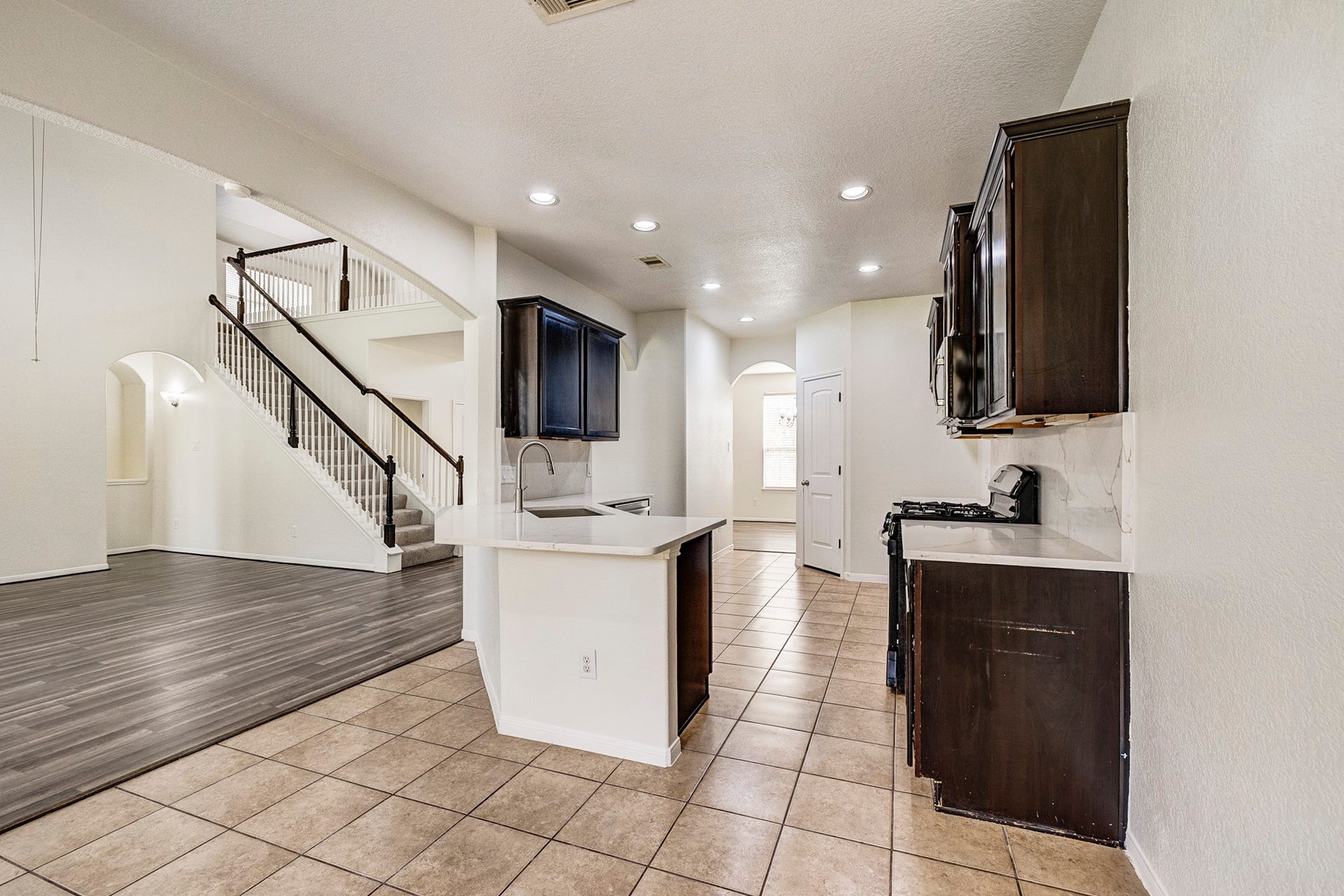 33227 Greenfield Forest Drive, Magnolia, TX 77354 Bright and open kitchen with dark cabinetry and modern fixtures, seamlessly connected to a spacious living area with elegant flooring and a stylish staircase.
