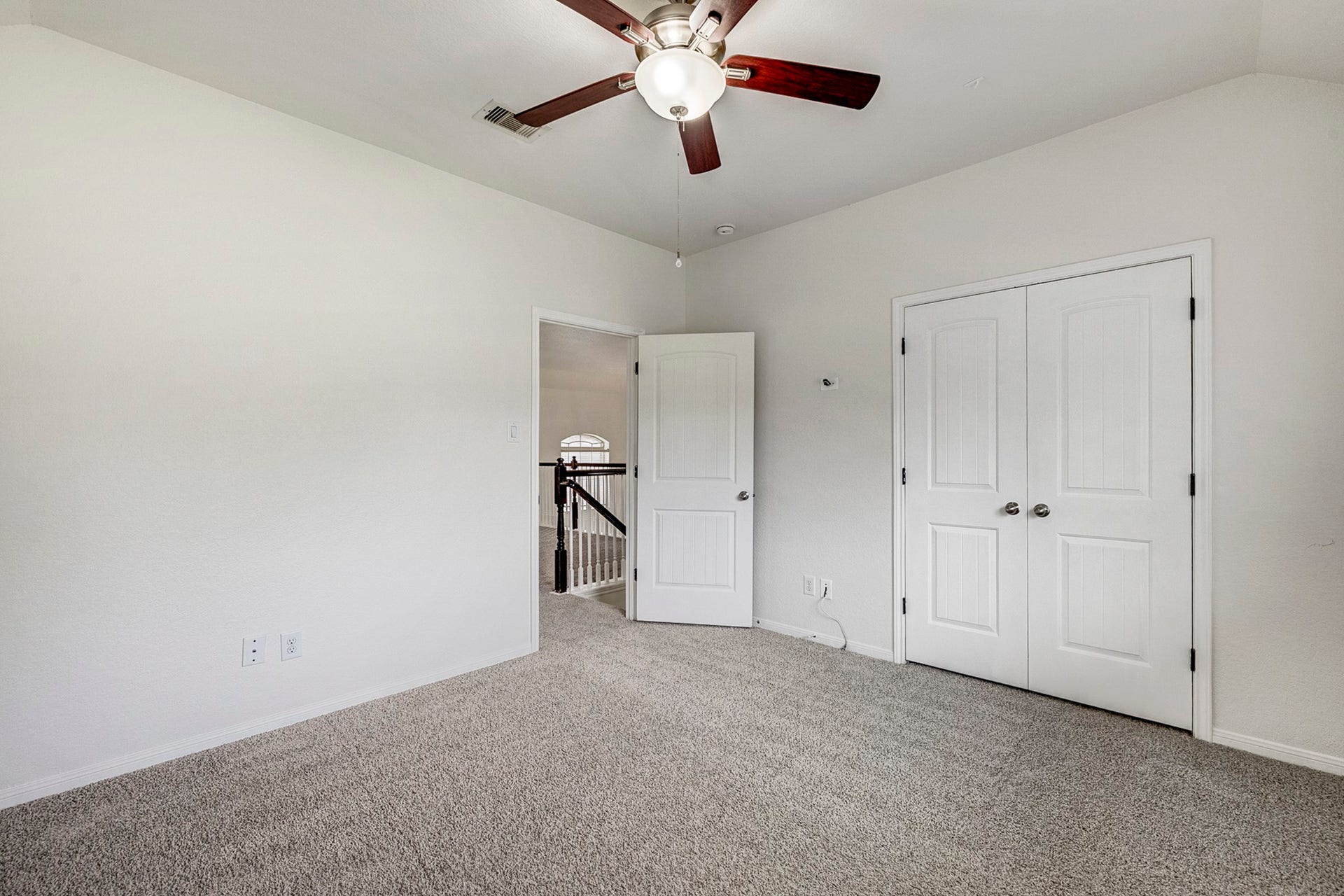 33227 Greenfield Forest Drive, Magnolia, TX 77354 Spacious room with soft carpeting, neutral walls, and a ceiling fan, featuring a double-door closet and an open doorway leading to a hallway with elegant railings.