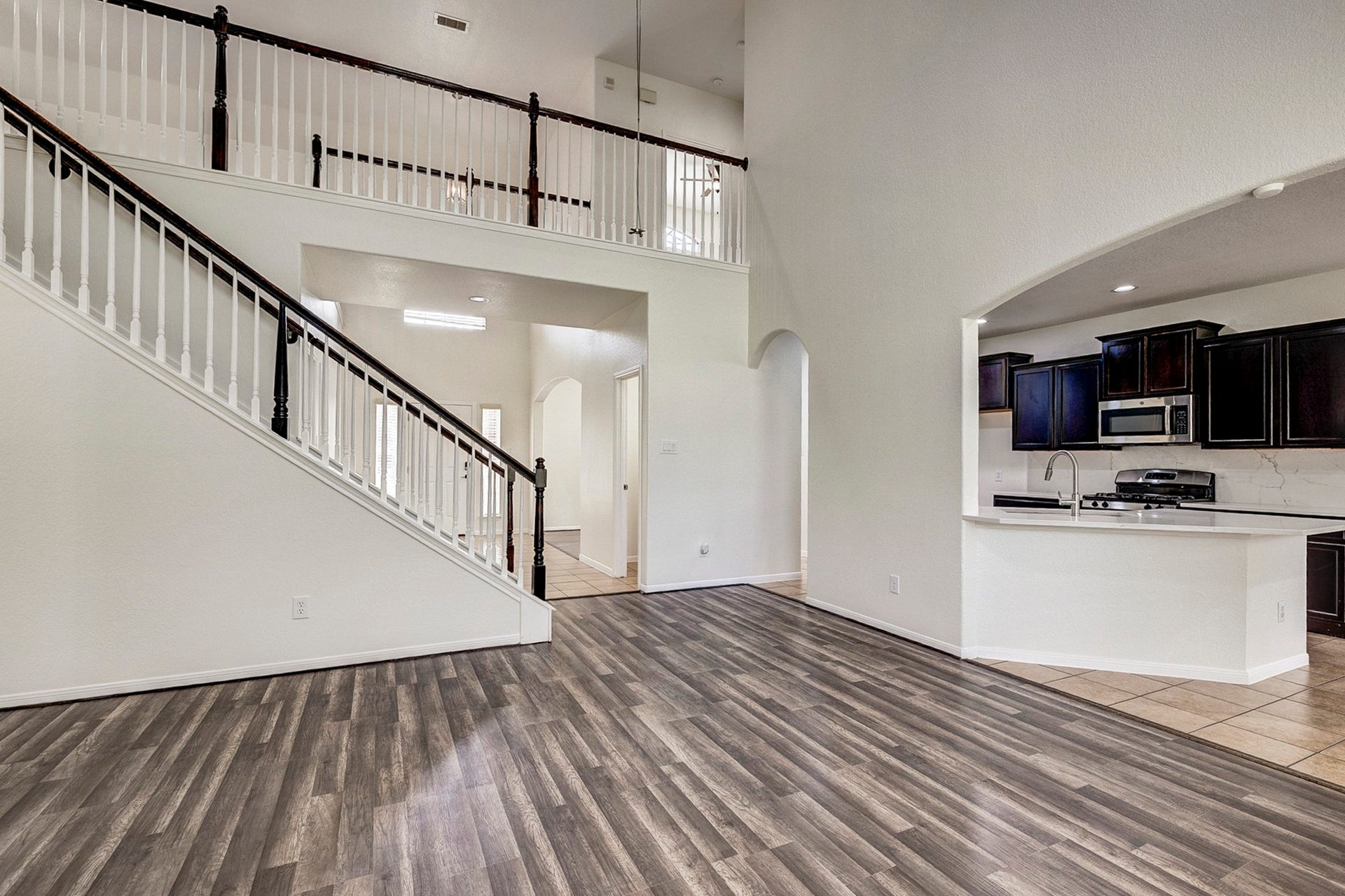 33227 Greenfield Forest Drive, Magnolia, TX 77354 Spacious open-concept living area featuring elegant wood flooring, a dramatic staircase, and a modern kitchen with dark cabinetry and stainless steel appliances.