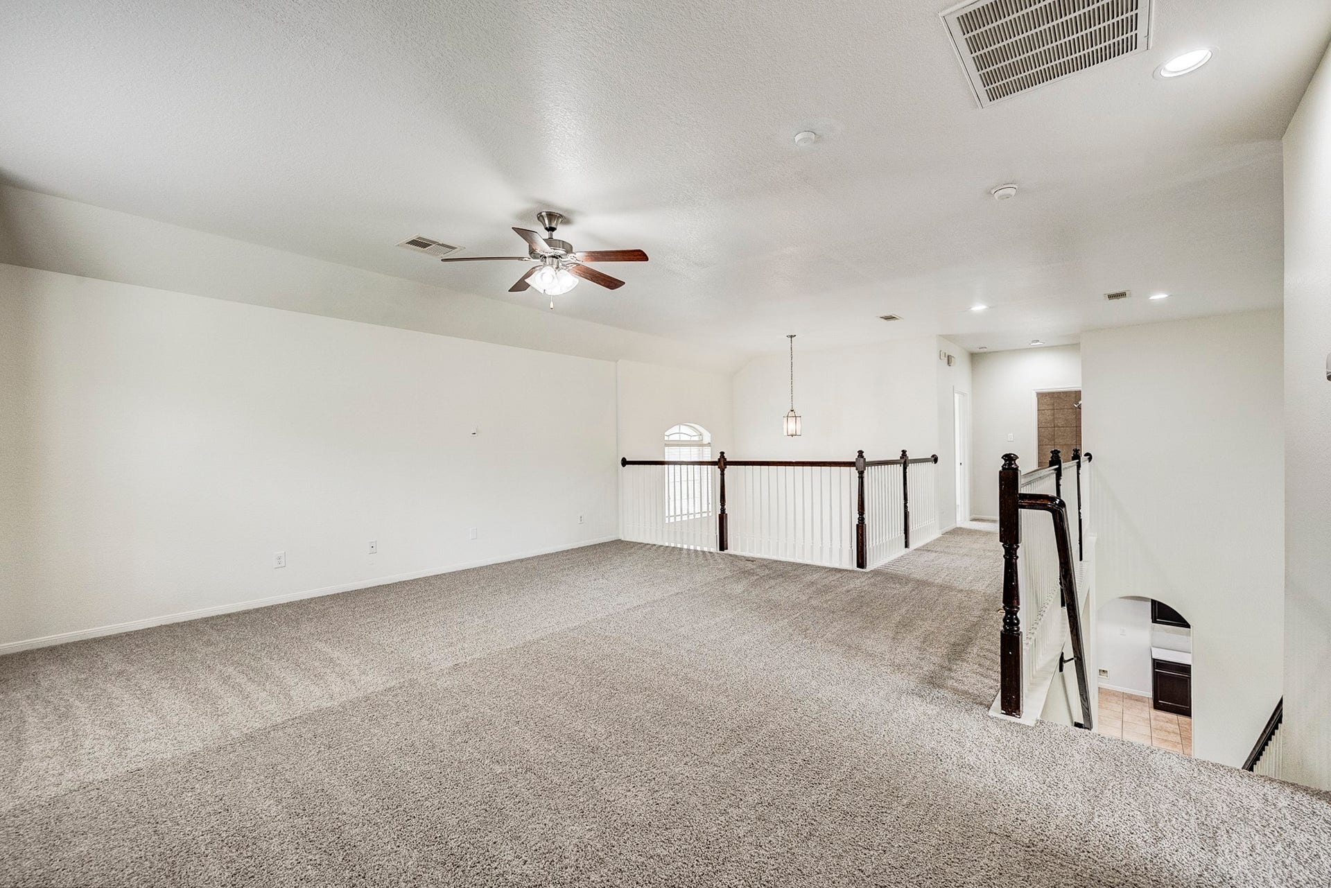 33227 Greenfield Forest Drive, Magnolia, TX 77354 Spacious and airy loft area with plush carpeting, ceiling fan, and elegant railing, perfect for a versatile living space or office.