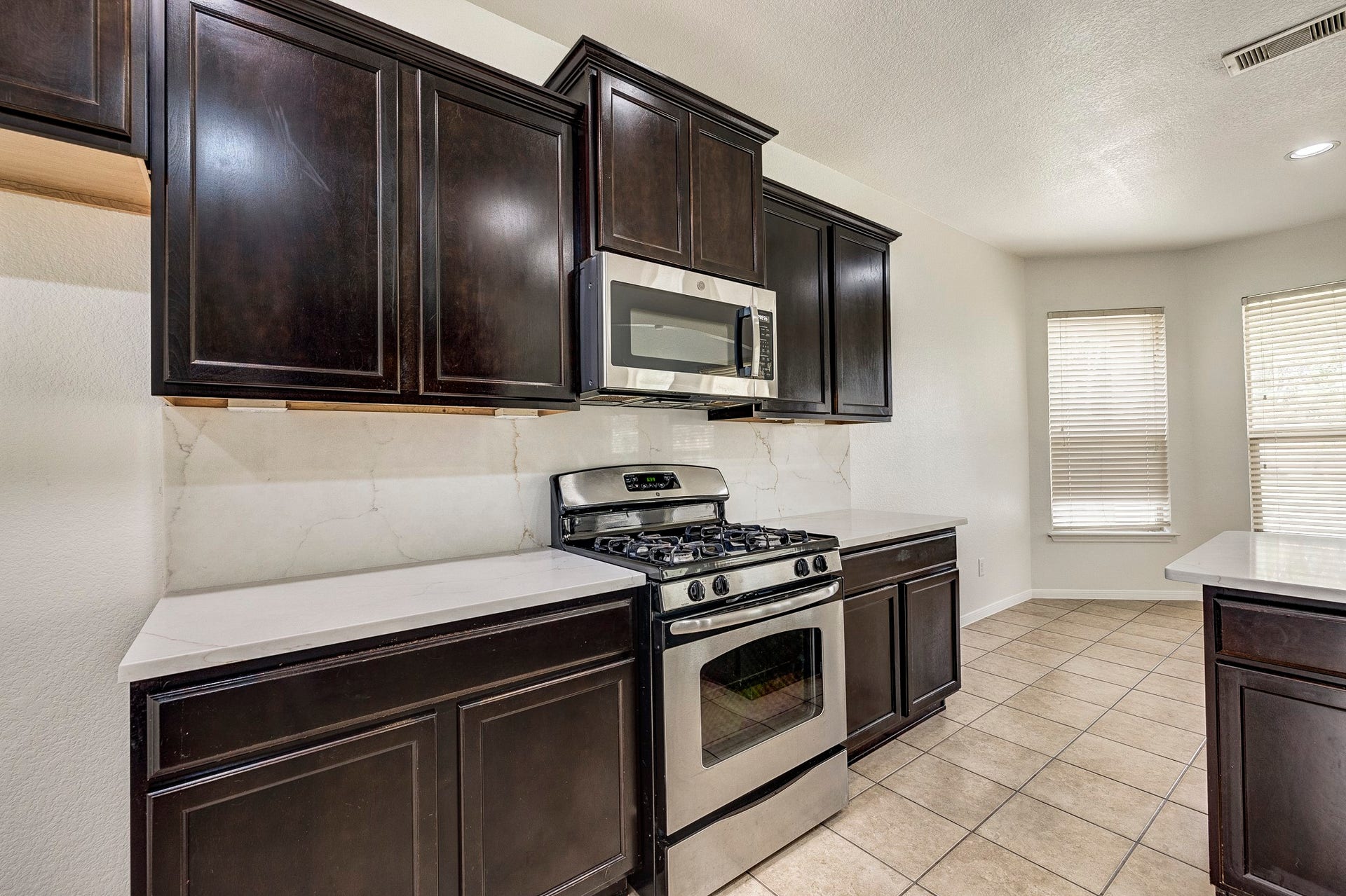 33227 Greenfield Forest Drive, Magnolia, TX 77354 Modern kitchen featuring dark wood cabinets, sleek stainless steel appliances, and a bright dining area with large windows.