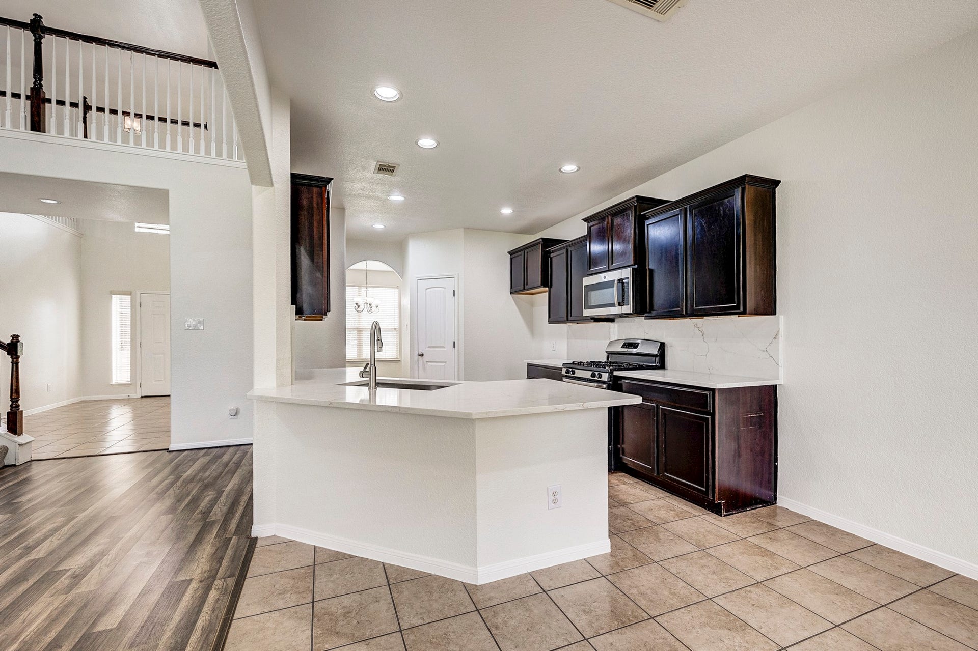 33227 Greenfield Forest Drive, Magnolia, TX 77354 Modern kitchen with sleek dark cabinetry, stainless steel appliances, and a spacious white countertop. Open layout leads to a bright entryway with elegant flooring and high ceilings.