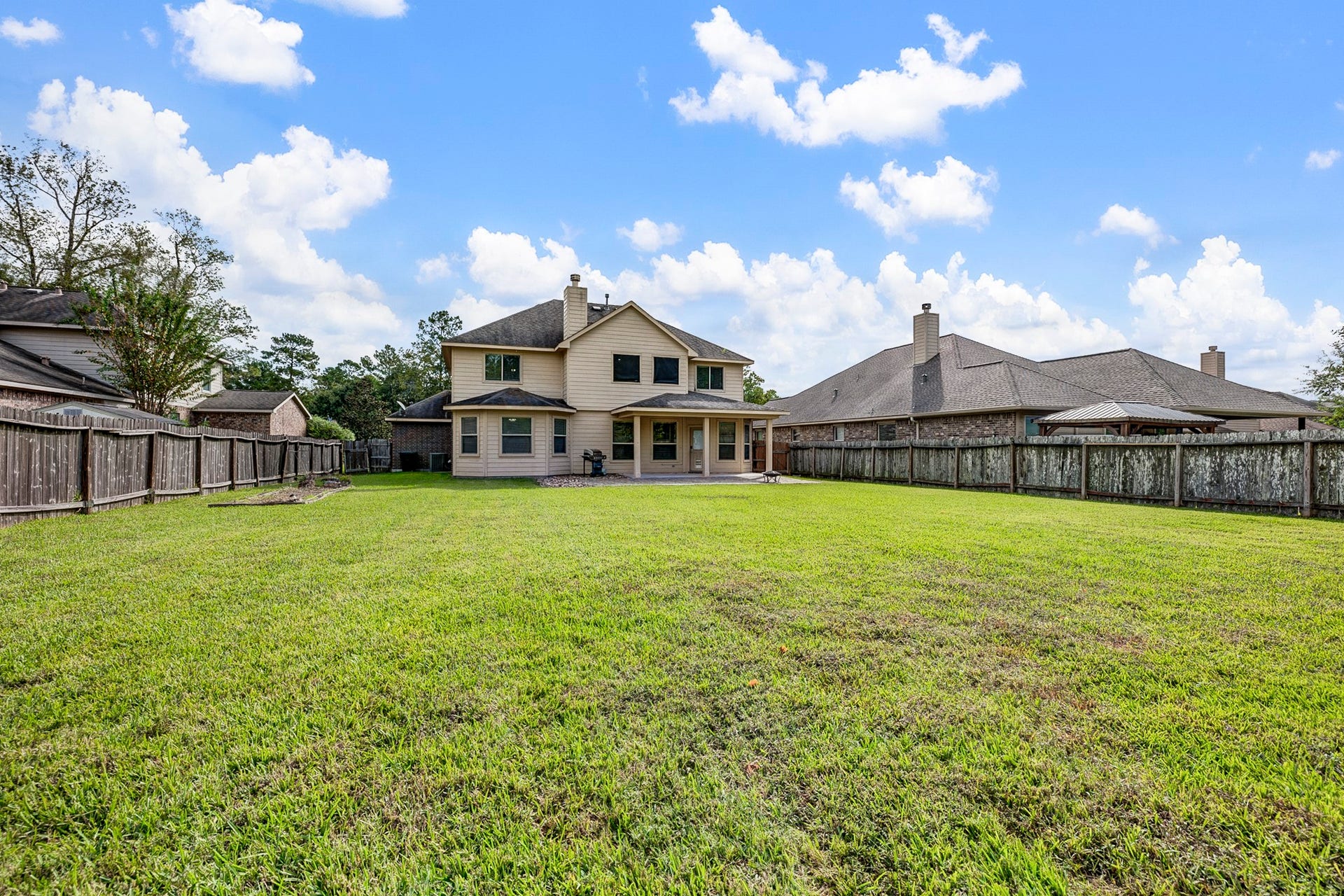 33227 Greenfield Forest Drive, Magnolia, TX 77354 Expansive backyard with lush green lawn, perfect for outdoor activities and entertaining, complemented by a charming two-story home.