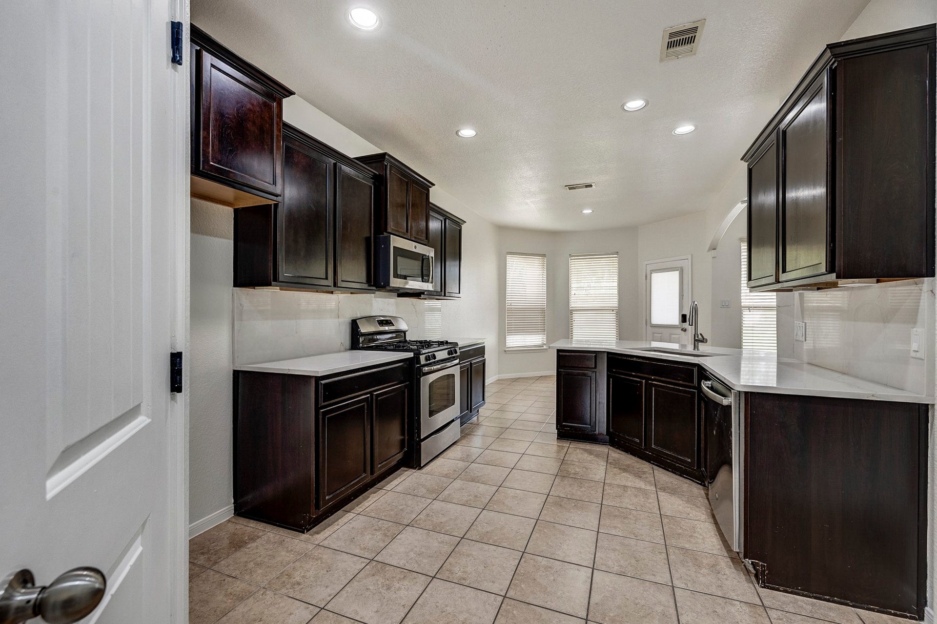 33227 Greenfield Forest Drive, Magnolia, TX 77354 Spacious kitchen with rich dark cabinetry, modern stainless steel appliances, and elegant tiled flooring, complemented by abundant natural light from large windows.