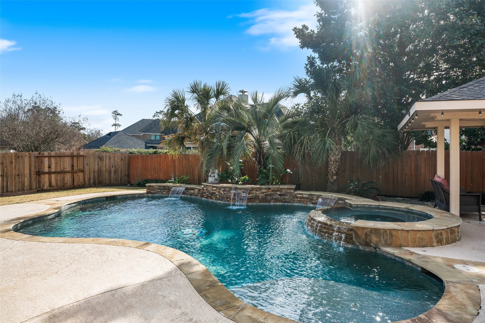 14318 Red Creek Cove Lane, Humble, TX 77396 Backyard features a beautifully designed pool with water feature that is connected hot tub, surrounded by palm trees and a privacy fence, creating a perfect oasis for relaxation and entertainment.
