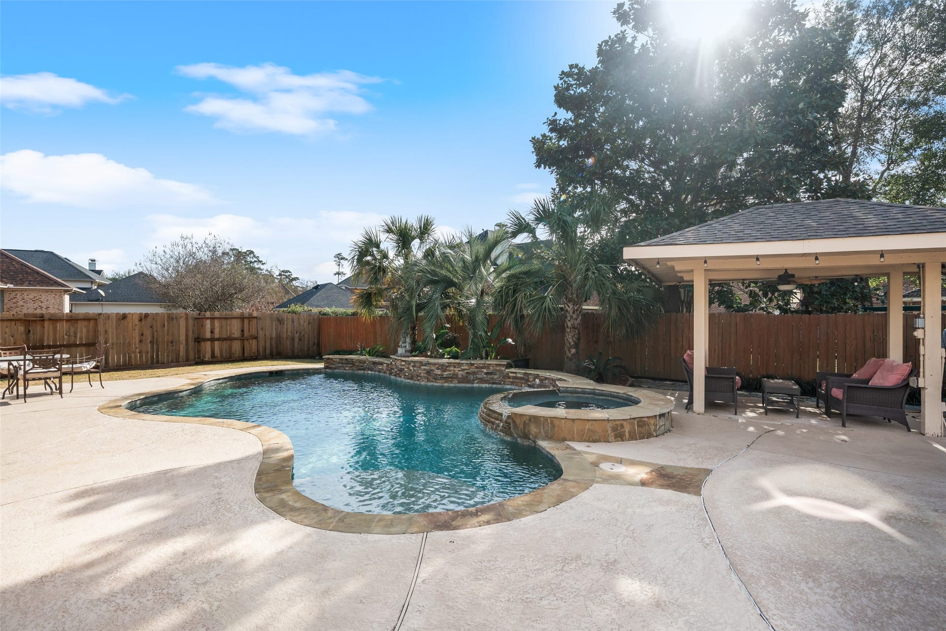 14318 Red Creek Cove Lane, Humble, TX 77396 Backyard features a spacious pool with a built-in hot tub, surrounded by a patio area perfect for lounging. A wooden fence provides privacy, while a covered seating area offers shade. Ideal for outdoor relaxation and entertaining.
