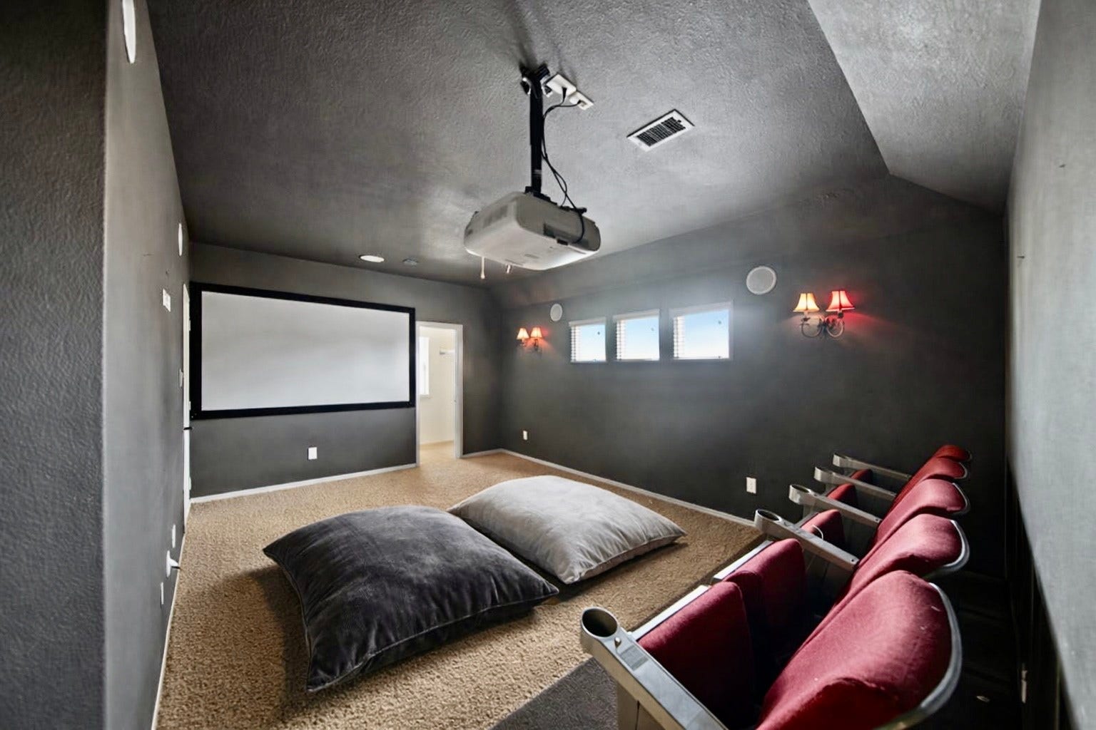 14318 Red Creek Cove Lane, Humble, TX 77396 Cozy home theater with dark walls features a ceiling-mounted projector, large screen, and comfortable seating. Carpeted flooring and small windows create an inviting atmosphere for movie nights.