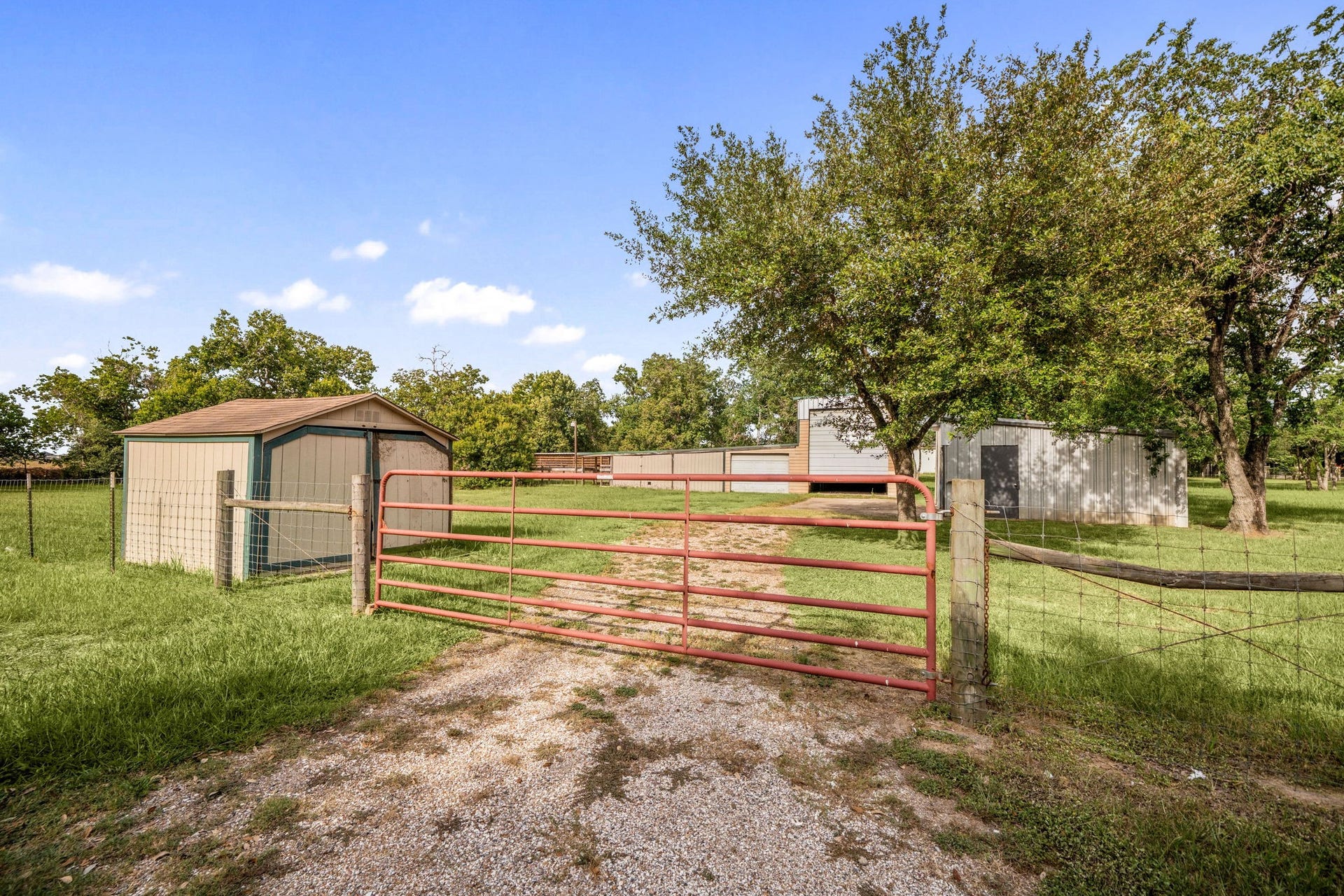 28310 Rose Lane, Katy, TX 77494 Highly functional acreage setup featuring a gated driveway entrance that opens up to versatile outbuildings, perfect for storage, projects, or hobby farming. The expansive, sun-drenched lot provides ample open space framed by mature trees and clear blue skies, offering a true country-living feel. This multi-use property layout is ideal for anyone needing extra room for equipment, workshops, or outdoor activities.