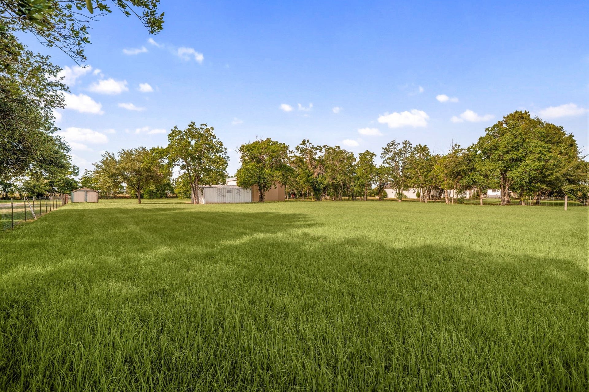 28310 Rose Lane, Katy, TX 77494 Expansive open pasture showcasing an incredible expanse of lush green grass, perfect for agricultural use, horses, or a custom homestead layout. A solid wood fence line runs along the perimeter of the field, which is beautifully accented by a distant border of mature hardwood trees. Under a wide-open blue sky, this sprawling acreage captures the true essence of peaceful country living and offers endless freedom for property expansion.