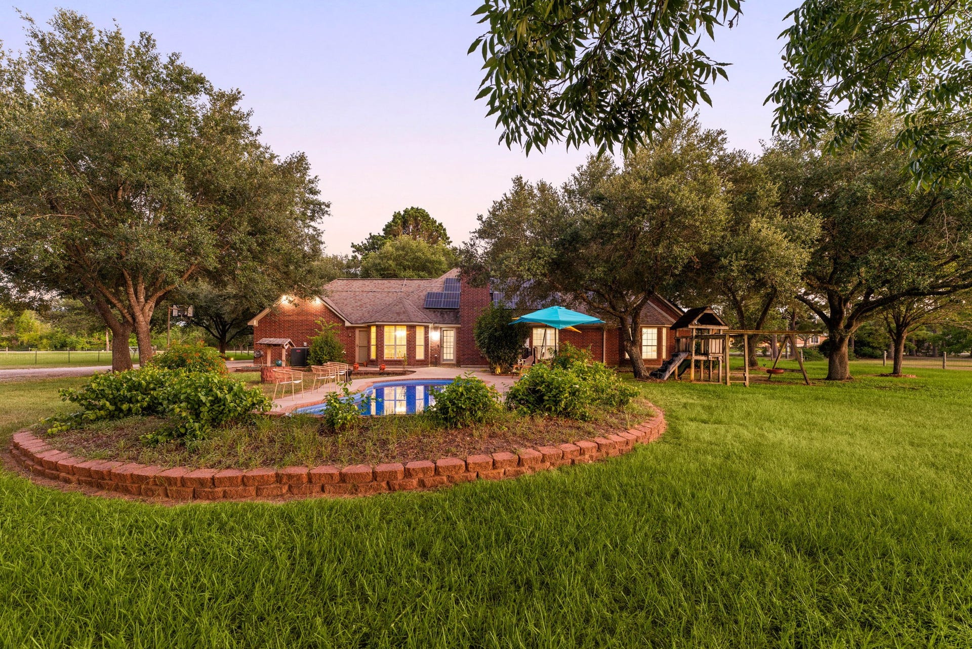 28310 Rose Lane, Katy, TX 77494 Impressive wide-angle view highlighting the sprawling lawn and an elegantly curved brick retaining wall that structures the poolside landscaping. This perspective showcases how the classic brick home, glistening in-ground pool, and expansive green spaces fit together harmoniously across the deep lot. Enveloped by towering mature trees, the property delivers an unmatched level of secluded country-style living while maintaining a clean, manicured presentation.