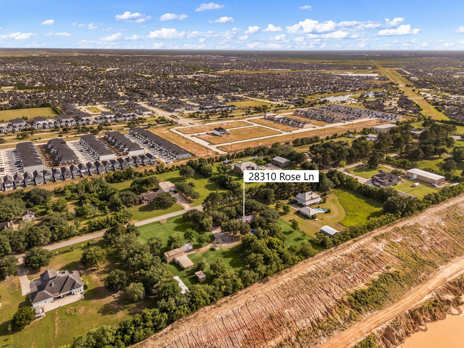 28310 Rose Lane, Katy, TX 77494 Breathtaking high-altitude aerial view showcasing the property's prime location, blending rural tranquility with suburban convenience. The property sits nestled on a beautifully wooded, expansive lot, with peaceful views of the green surroundings of the immediate acreage while revealing close proximity to developing master-planned communities, open skies, and major roadways.