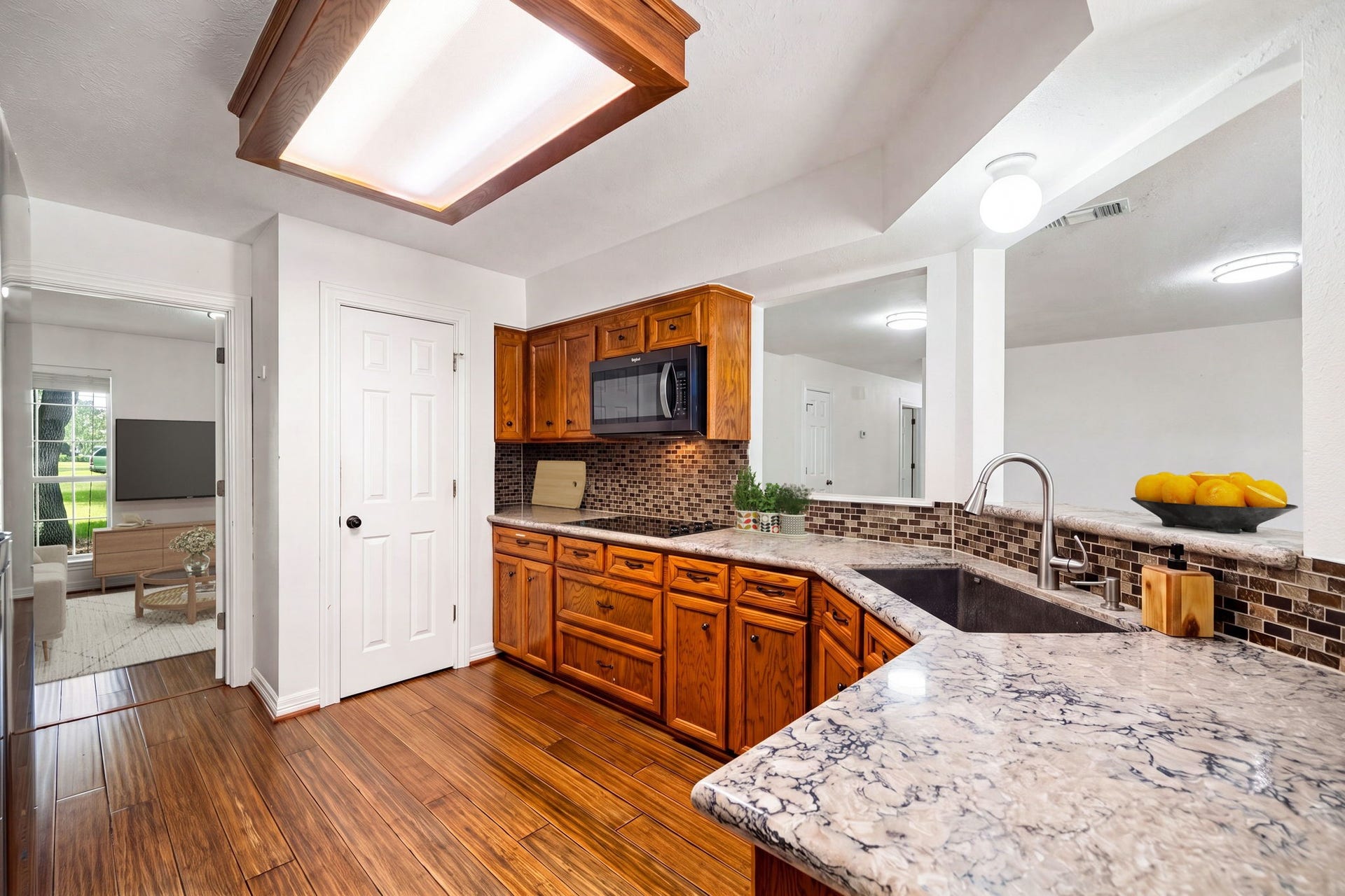 28310 Rose Lane, Katy, TX 77494 Well-appointed kitchen featuring warm wood cabinetry, premium granite countertops, and an undermount sink with a modern gooseneck faucet. The functional layout highlights an integrated cooktop, a built-in microwave, and continuous wood-look flooring that sweeps through into the living spaces. A raised breakfast bar pass-through looks out to the living areas, maintaining a bright and connected atmosphere.