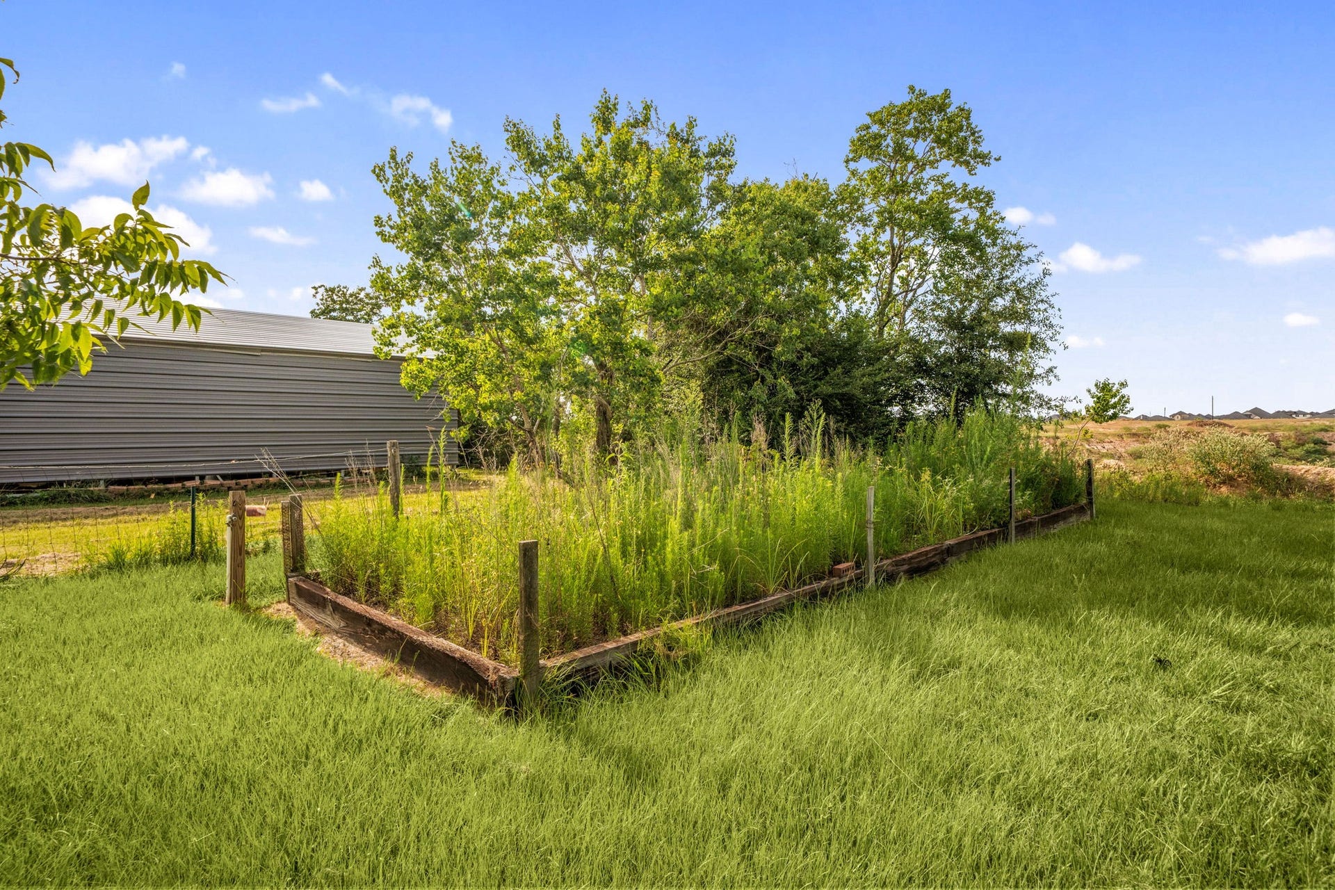 28310 Rose Lane, Katy, TX 77494 Charming backyard addition featuring a substantial, timber-enframed raised garden plot perfect for homesteading, home-grown vegetables, or custom landscaping. Positioned on a sprawling green lawn under wide open skies, this dedicated planting area is bordered by young shade trees and overlooks an expansive lot. A fantastic feature for gardening enthusiasts looking to cultivate their own farm-to-table lifestyle.
