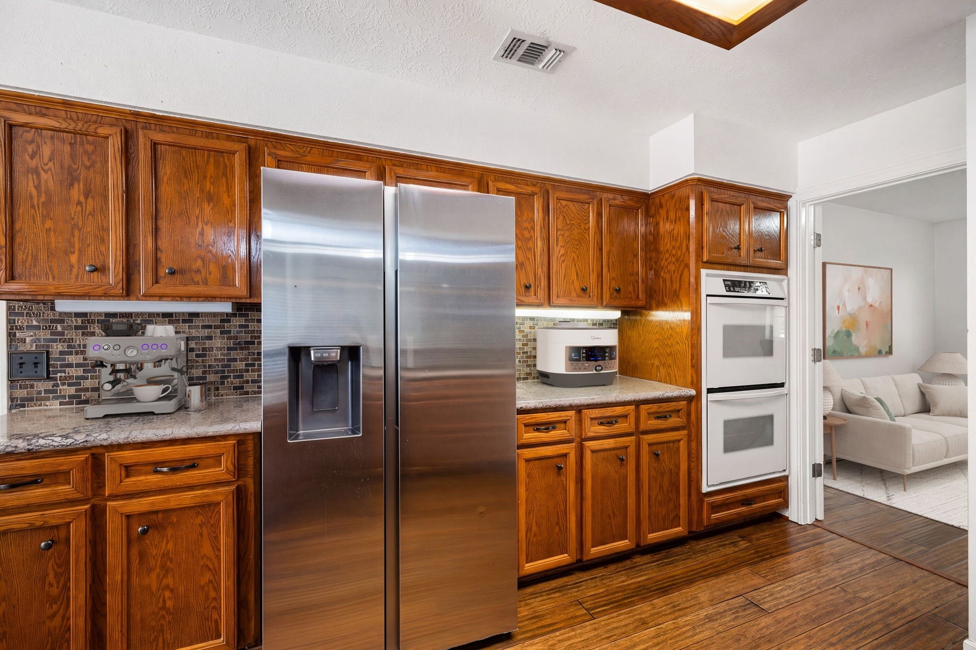 28310 Rose Lane, Katy, TX 77494 Efficient kitchen wall layout maximizing storage with a full suite of wood cabinetry and dedicated appliance stations. A stainless steel side-by-side refrigerator is flanked by counter space featuring an intricate tile backsplash and bright under-cabinet task lighting. The setup is completed by a built-in white double wall oven, offering premium cooking capacity right next to the open living area.